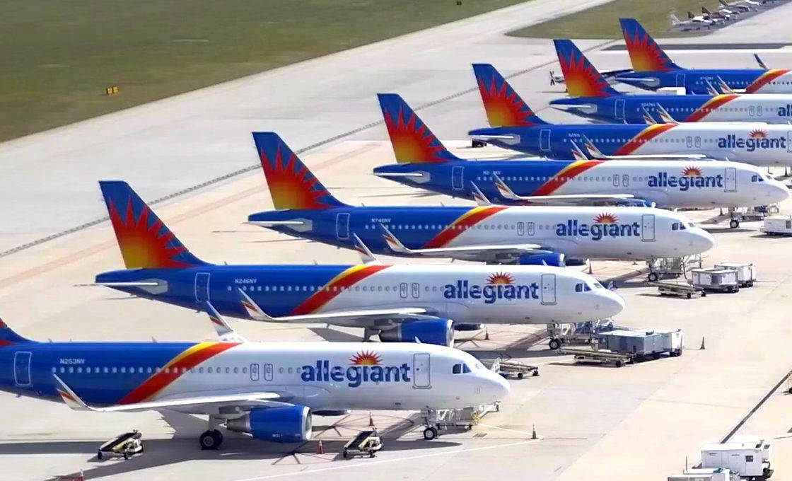transportation 桌布 壁紙 — 一排排 Allegiant Airlines 的噴射機，帶有藍橙色太陽爆發圖案的尾翼，停在陽光明媚的機場停機坪上。