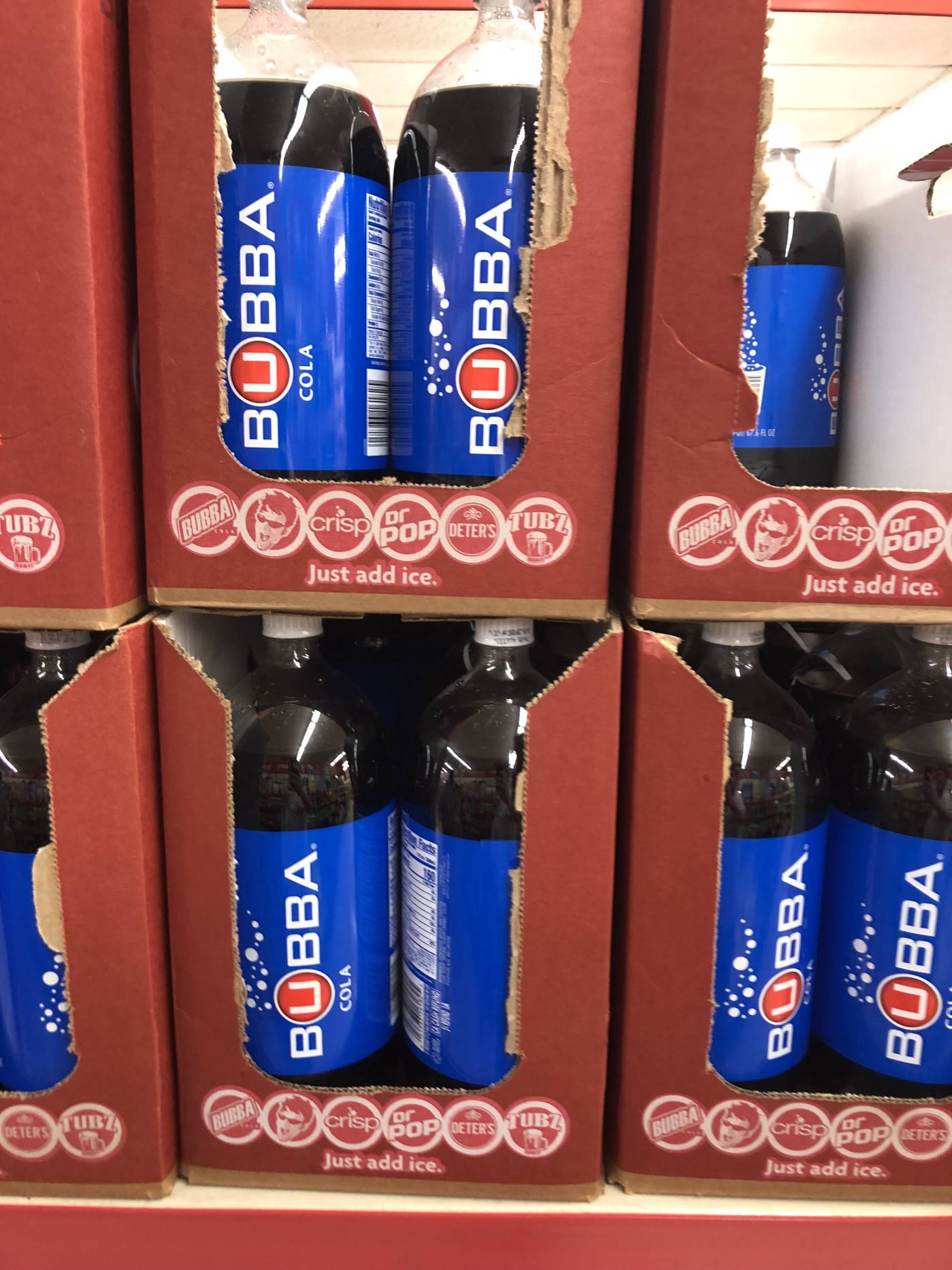 drinks 桌布 壁紙 — 一排排Bubba Cola瓶裝在紅色紙箱中，上面印有'Just add ice'標語，陳列在商店走道。