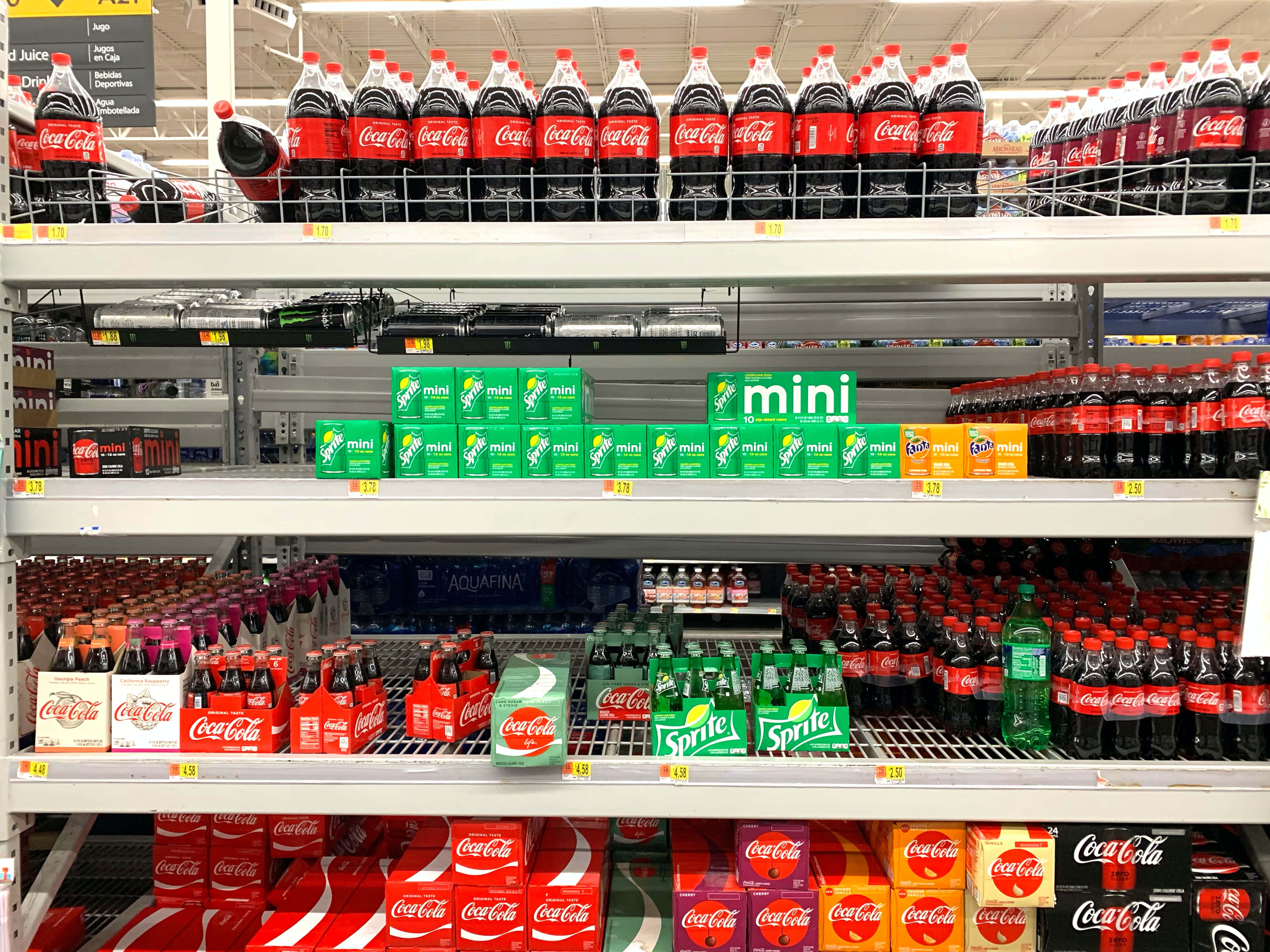 高清 桌布 壁紙 — 一排排Coca-Cola Sprite和Aquafina的瓶子和盒子整齊地排列在明亮的超市貨架上，在螢光燈下。