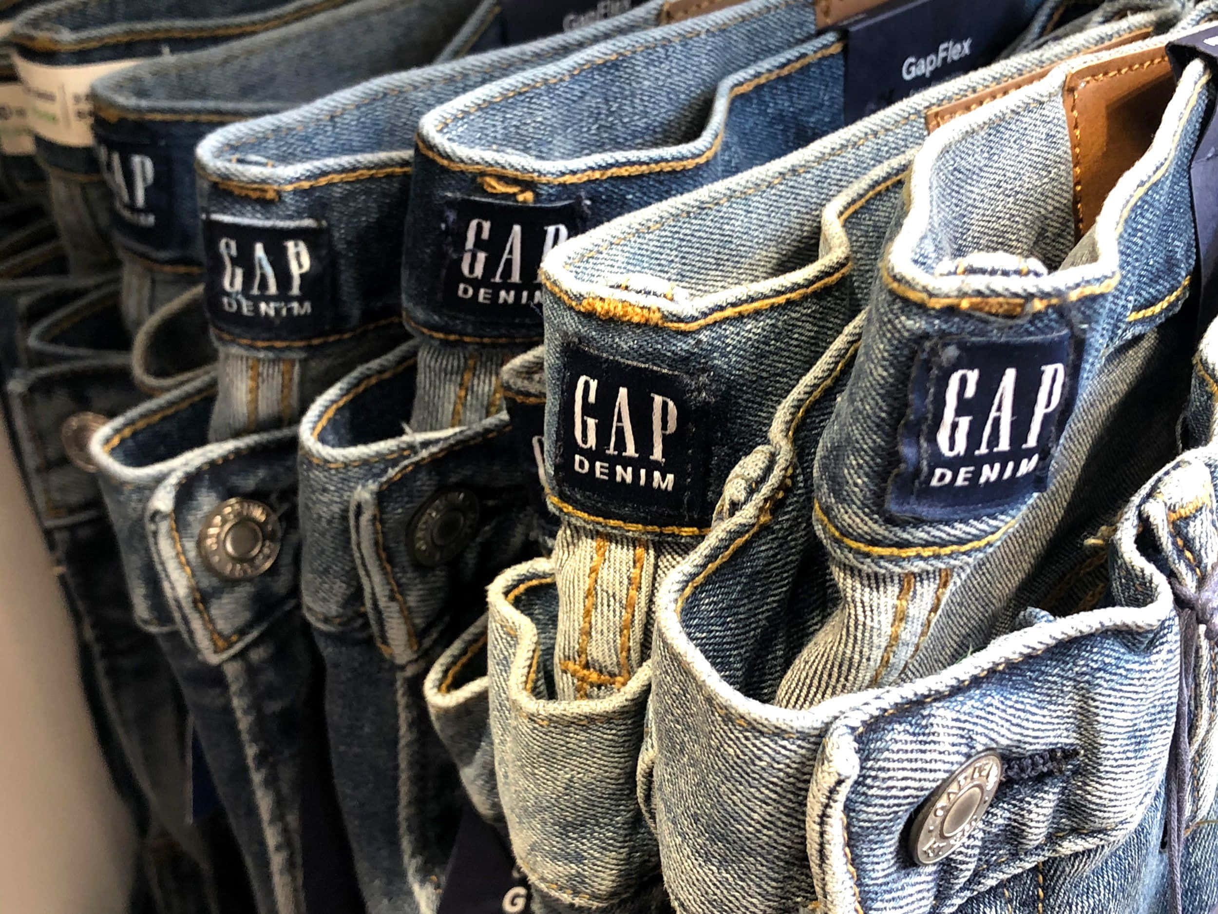 Gap 桌布 壁紙 — 一排排Gap牛仔褲整齊地掛在零售店中，展示藍色水洗和品牌標籤。