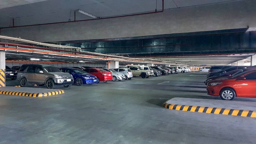 汽車 桌布 壁紙 — 一排排停泊的汽車，位於燈光昏暗的多層混凝土停車場，帶有黃黑相間的條紋路緣。