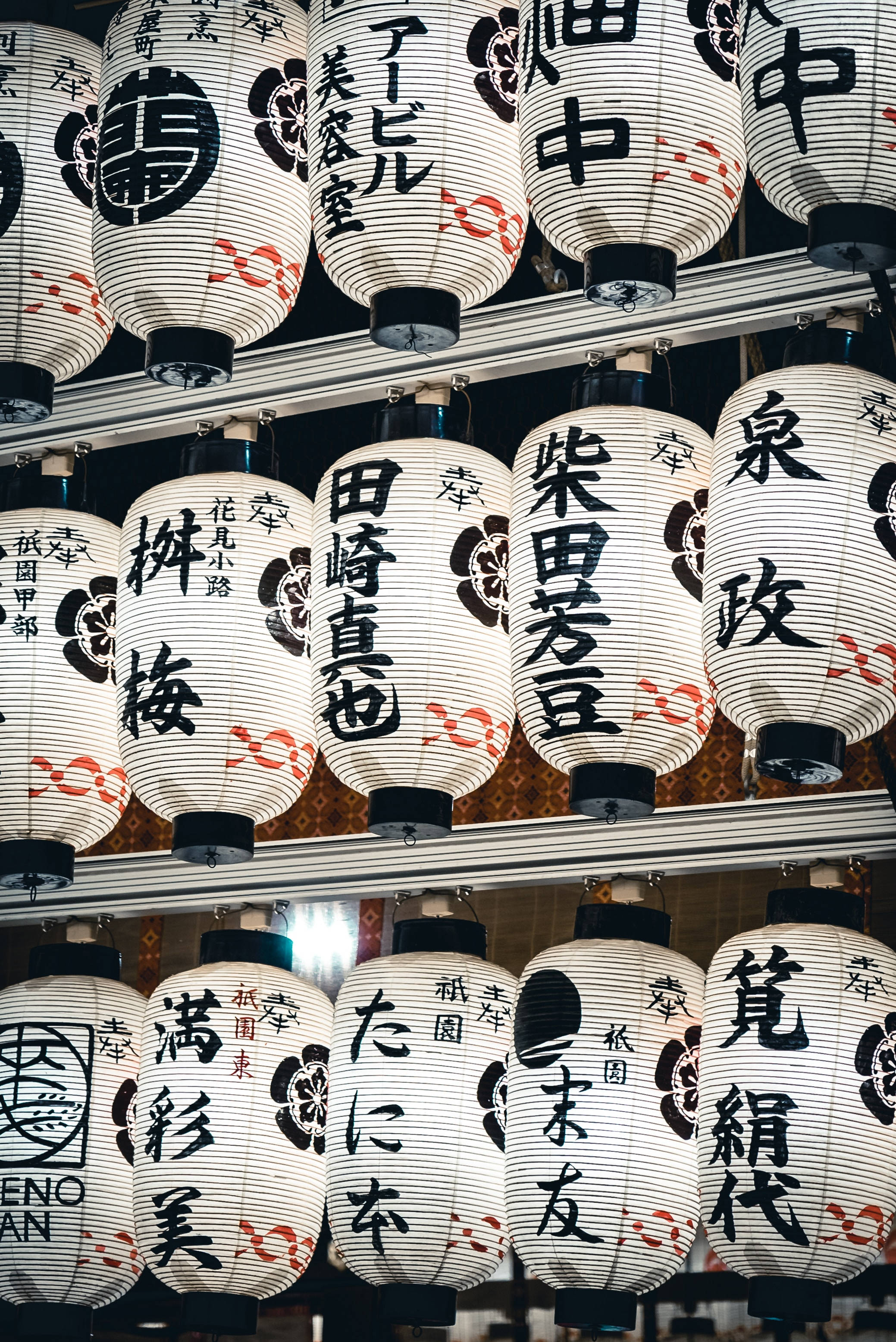 中文 桌布 壁紙 — 一排排傳統日本紙燈籠，上面有黑色和紅色的漢字，在黑暗的背景下懸掛著發光。