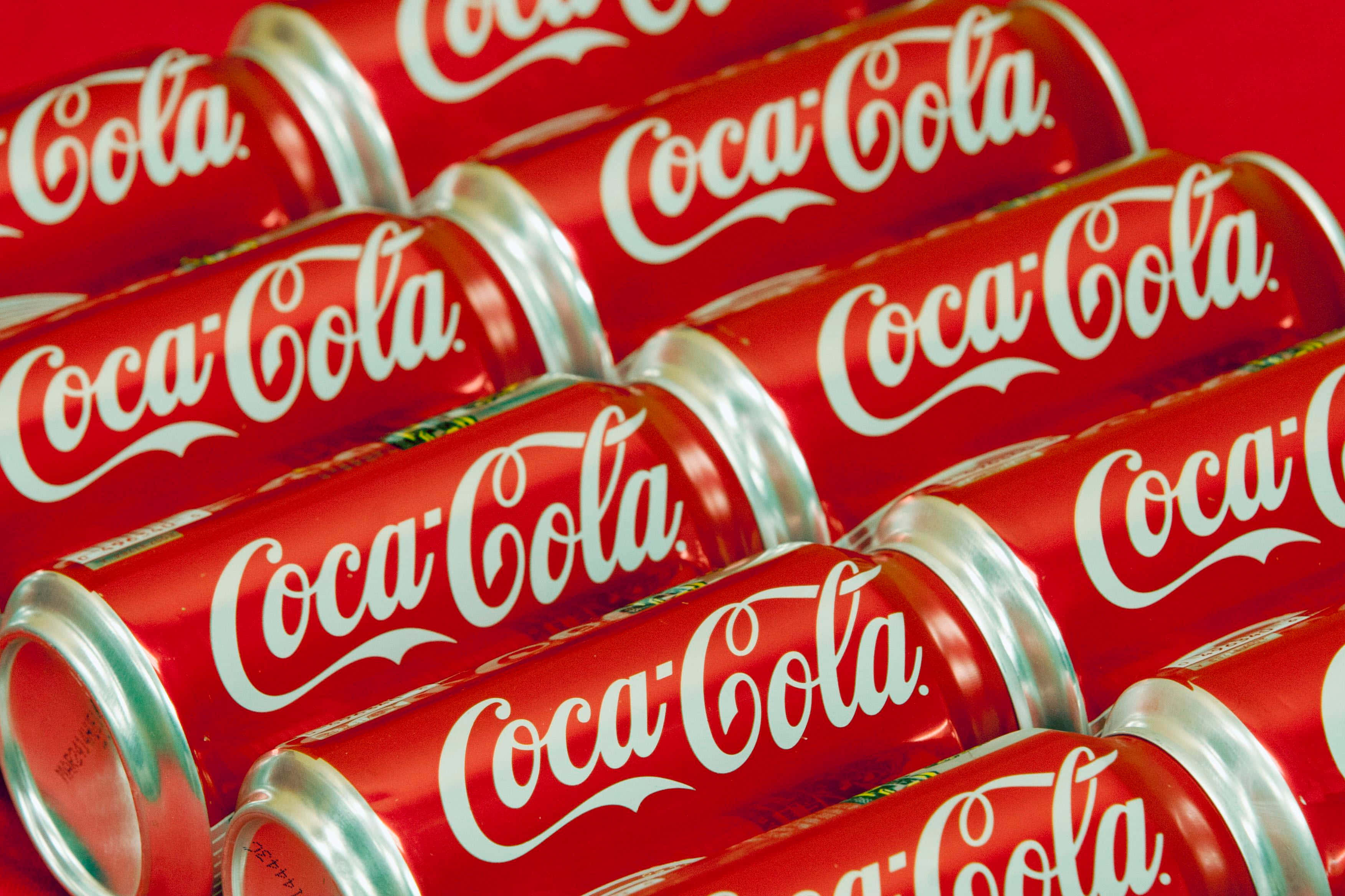 coca cola 桌布 壁紙 — 一排排光澤的紅色可口可樂罐，帶有白色草書標誌，對角線排列成緊密圖案。