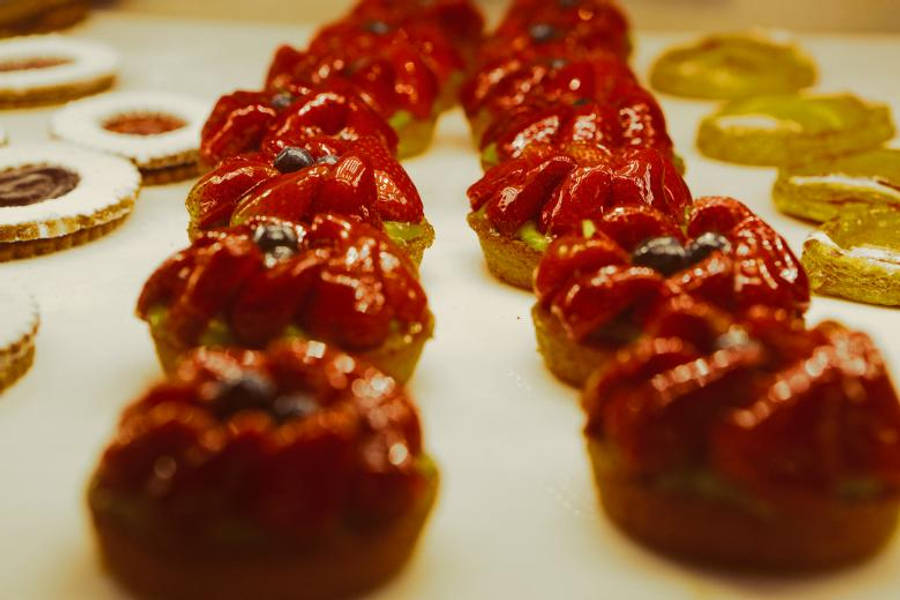 Pastries 桌布 壁紙 — 一排排光澤的紅色草莓塔配深色漿果，旁邊是金色奇異果片，放在白色表面上。