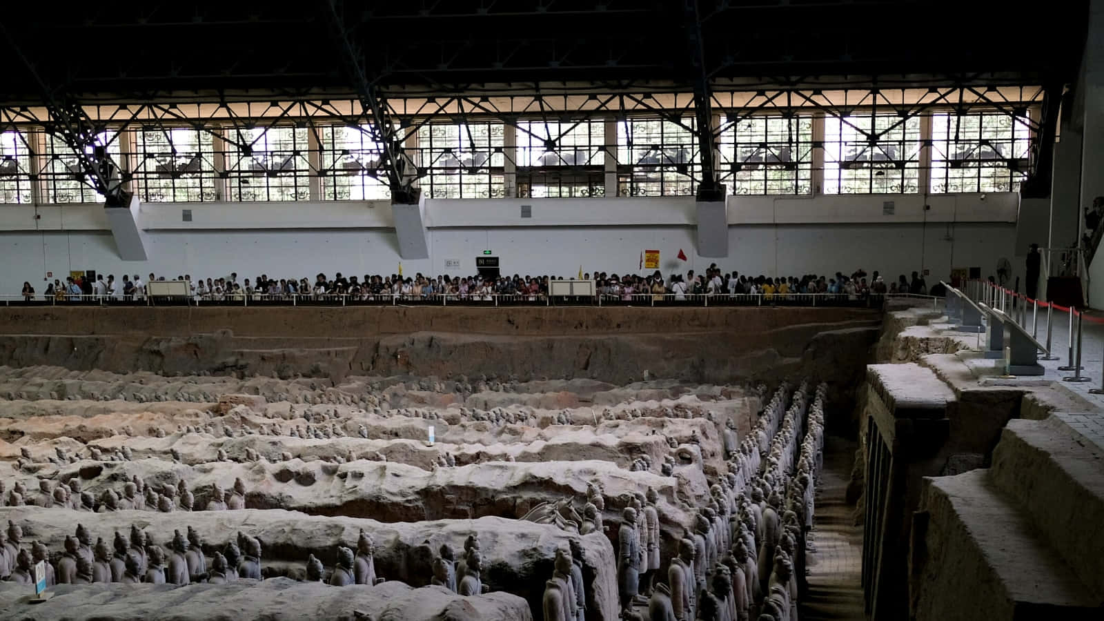 Museum 桌布 壁紙 — 一排排古代兵馬俑矗立在寬闊的博物館發掘坑中，遊客從高架步道上觀看。