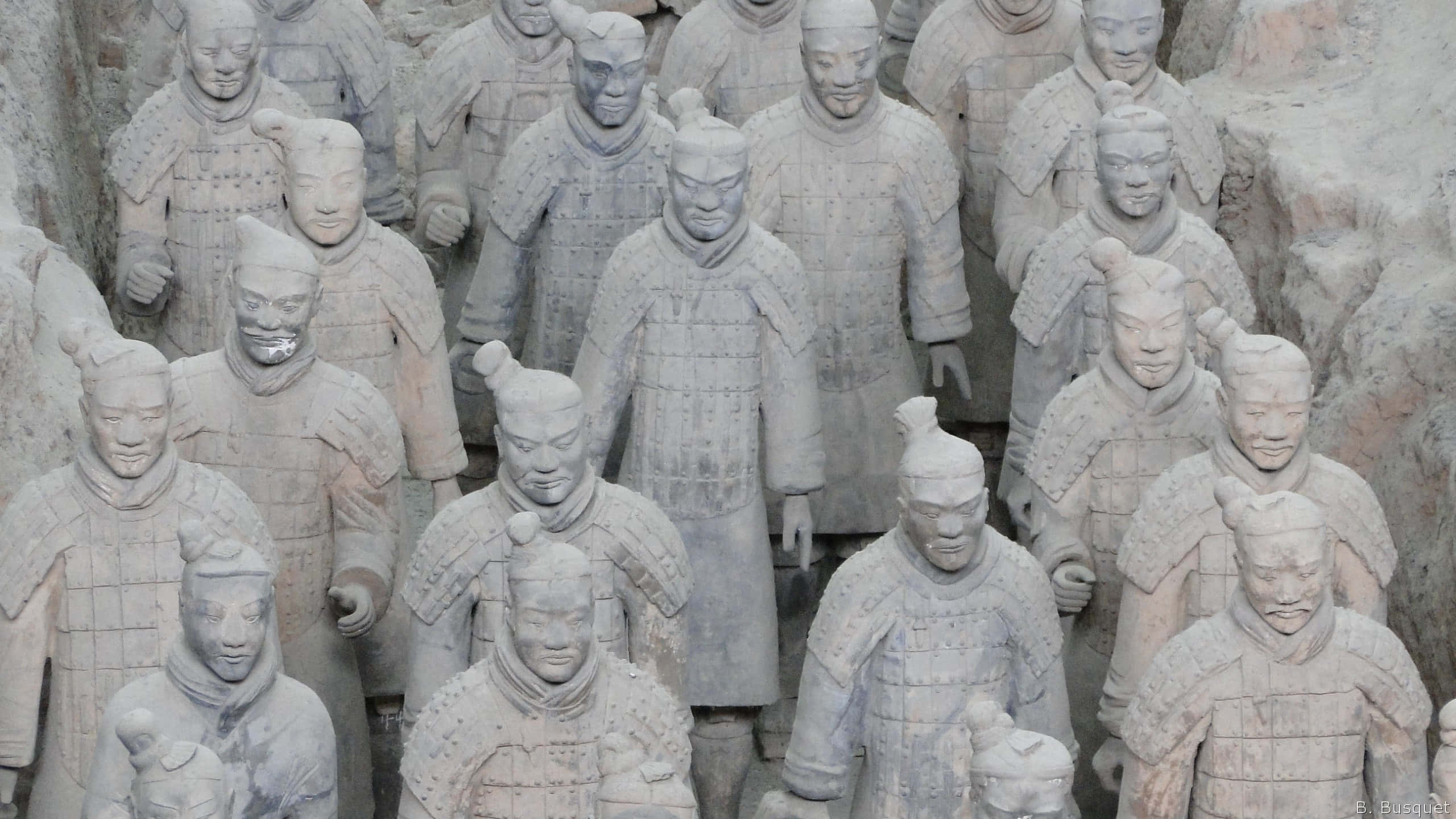 Museum 桌布 壁紙 — 一排排古老的兵馬俑以大地色調站立，帶有精細的盔甲和莊嚴的表情。
