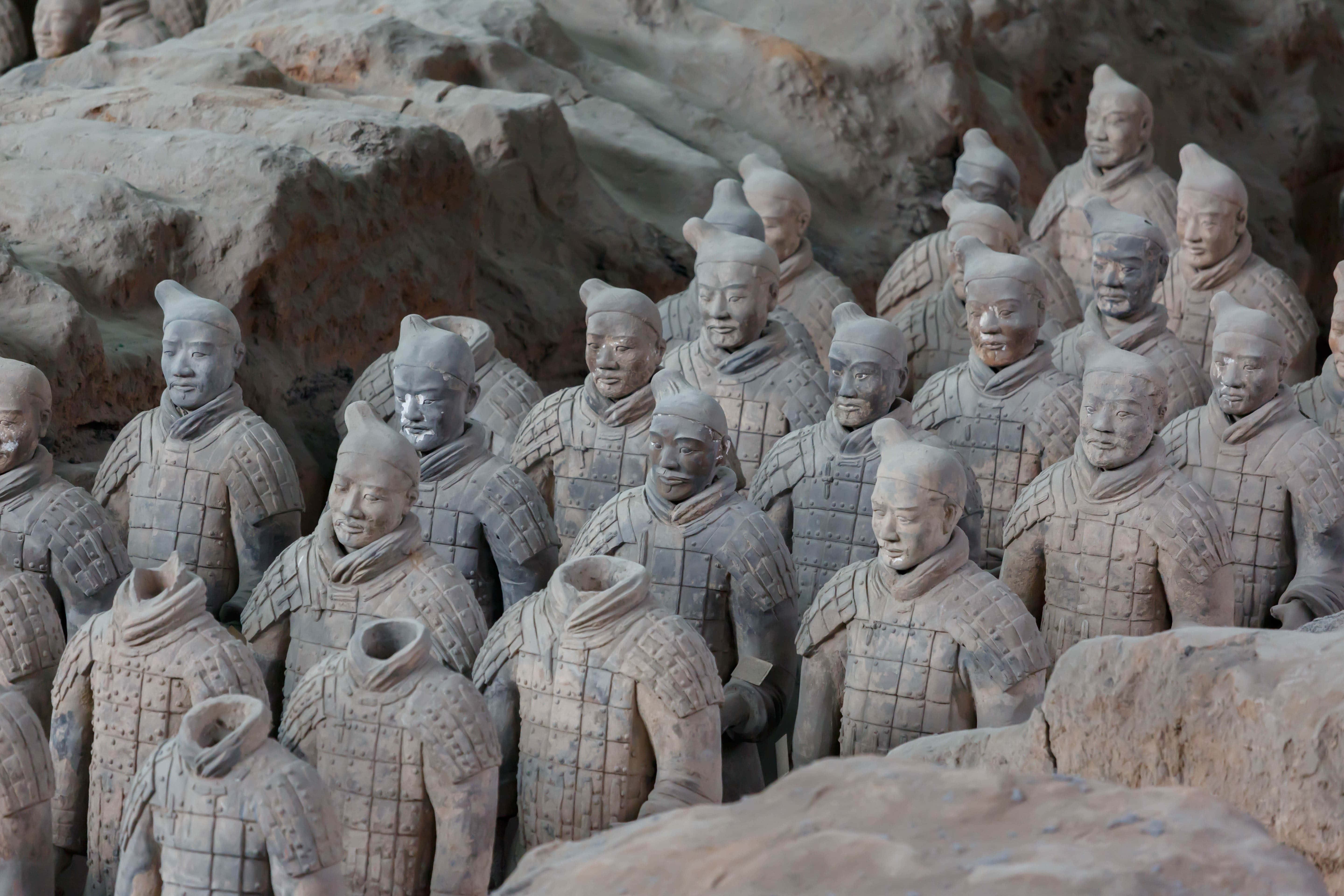 Museum 桌布 壁紙 — 一排排古老的兵馬俑以大地色調站立在發掘坑內，每個都有獨特的面部表情和詳細的盔甲。