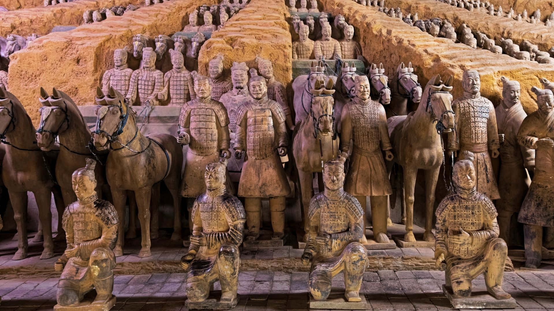 Museum 桌布 壁紙 — 一排排古老的兵馬俑在溫暖的燈光下，於考古發掘現場整齊排列。