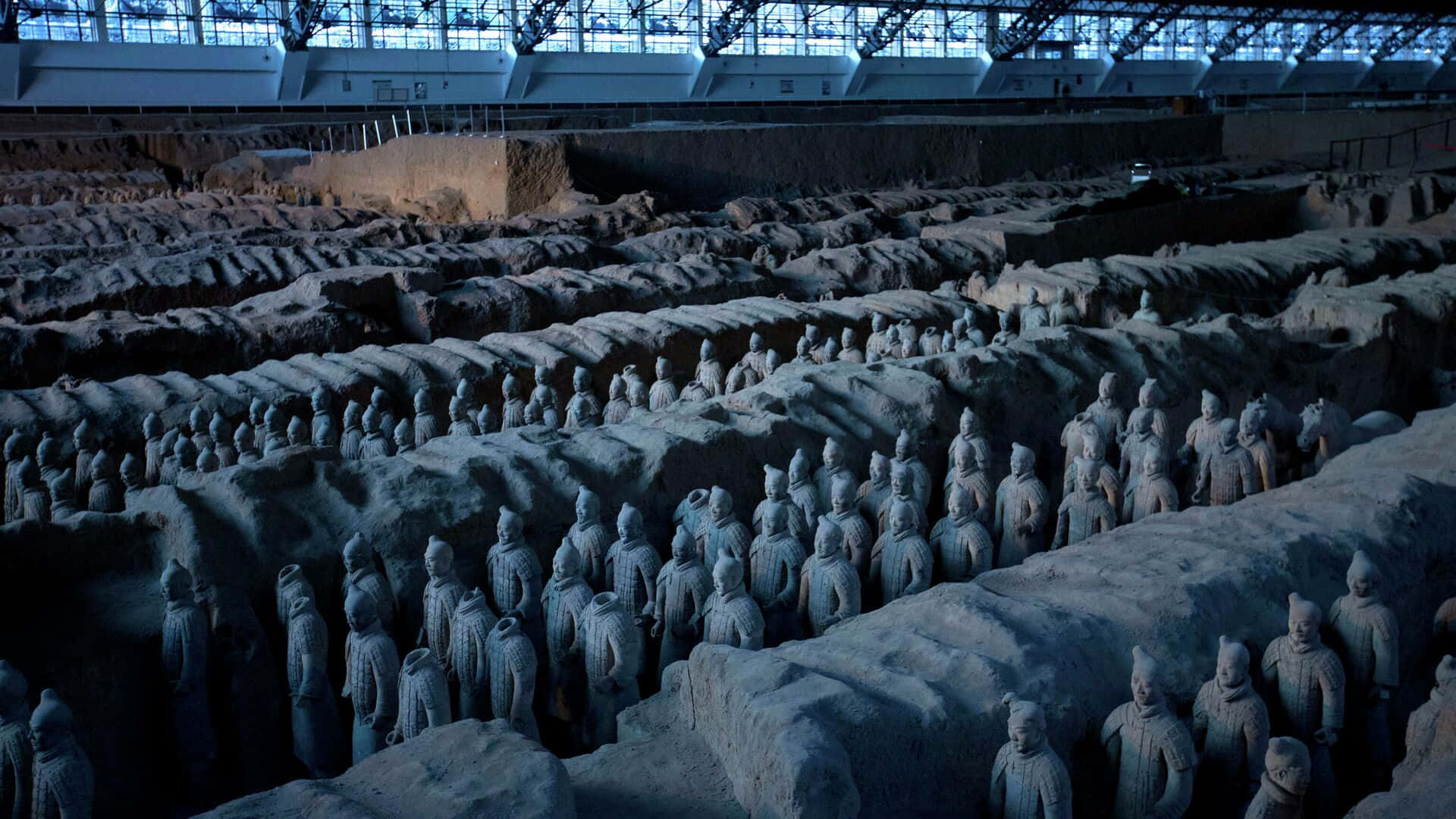 Museum 桌布 壁紙 — 一排排古老的兵馬俑在現代保護屋頂下，於其龐大的考古發掘現場中列隊站立。