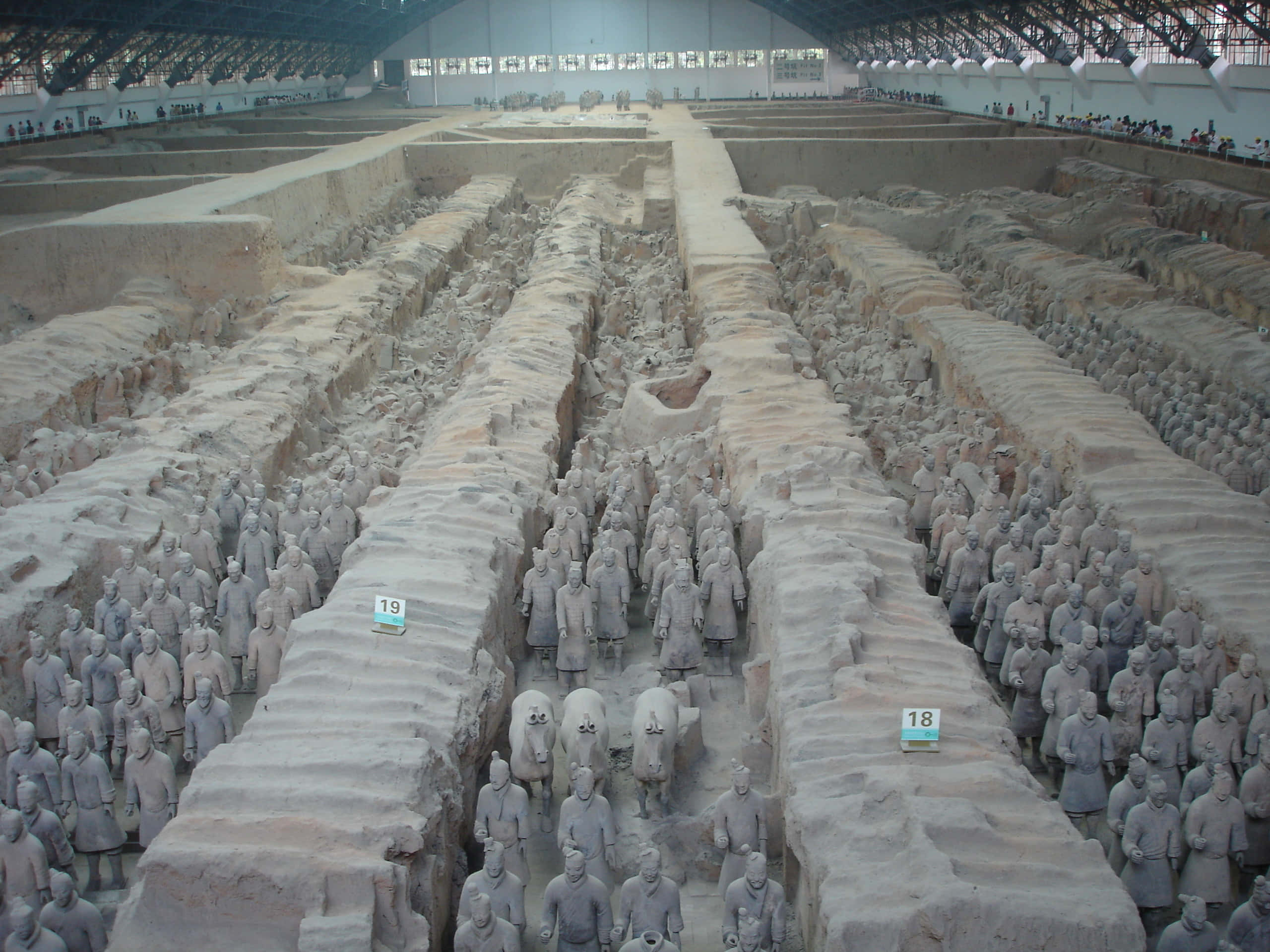 Museum 桌布 壁紙 — 一排排古老的兵馬俑在現代保護屋頂下的廣闊考古發掘現場中列隊站立。