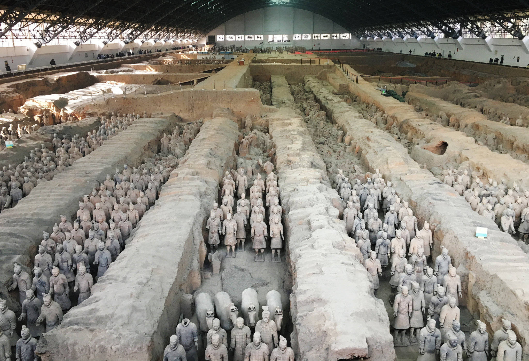 中國 桌布 壁紙 — 一排排古老的兵馬俑在現代保護屋頂下的廣闊兵馬俑發掘坑中列隊站立。