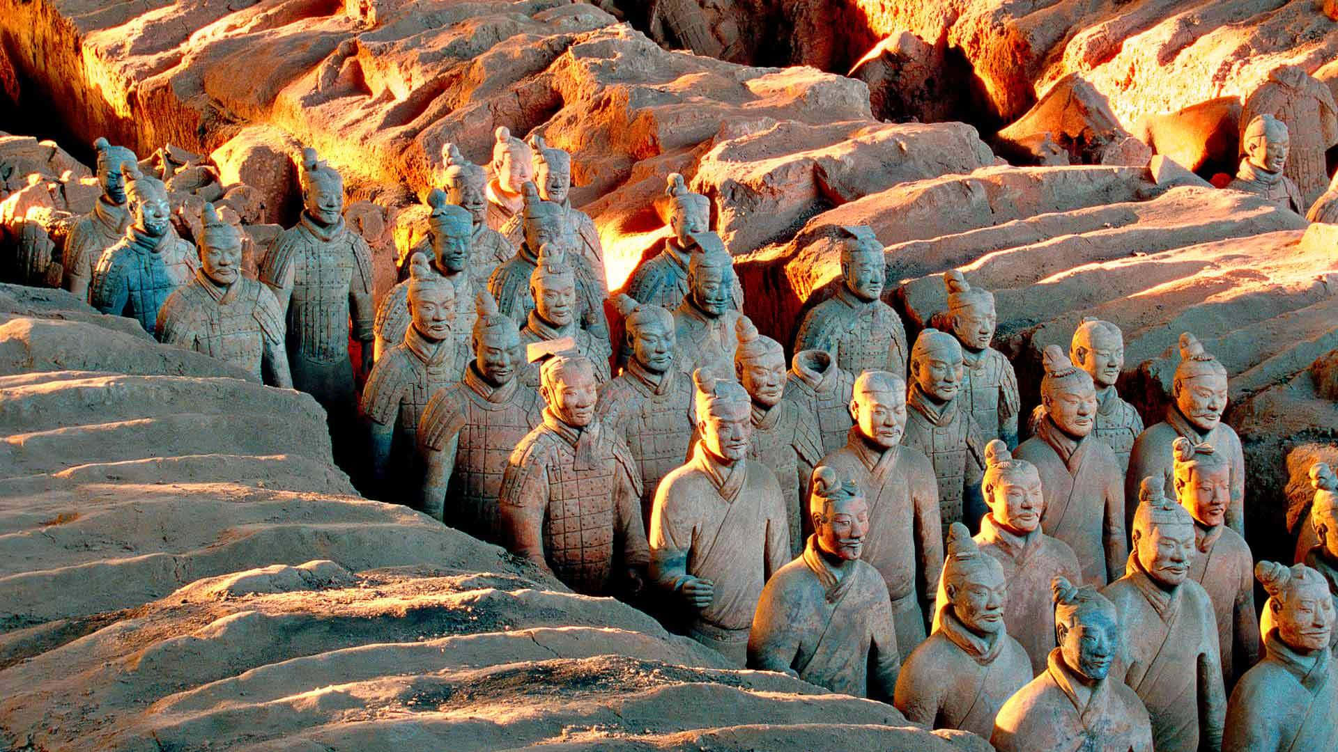 Museum 桌布 壁紙 — 一排排古老的兵馬俑從泥土戰壕中浮現，沐浴在溫暖的金色夕陽光中。
