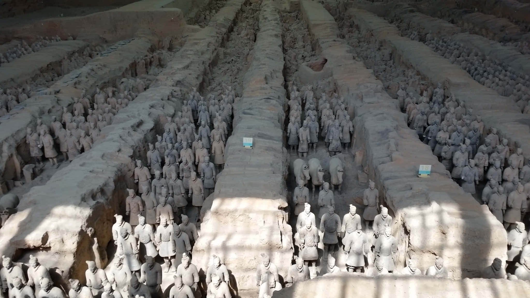 Museum 桌布 壁紙 — 一排排古老的兵馬俑整齊地排列在泥土掩埋的坑內，沐浴在自然光中。