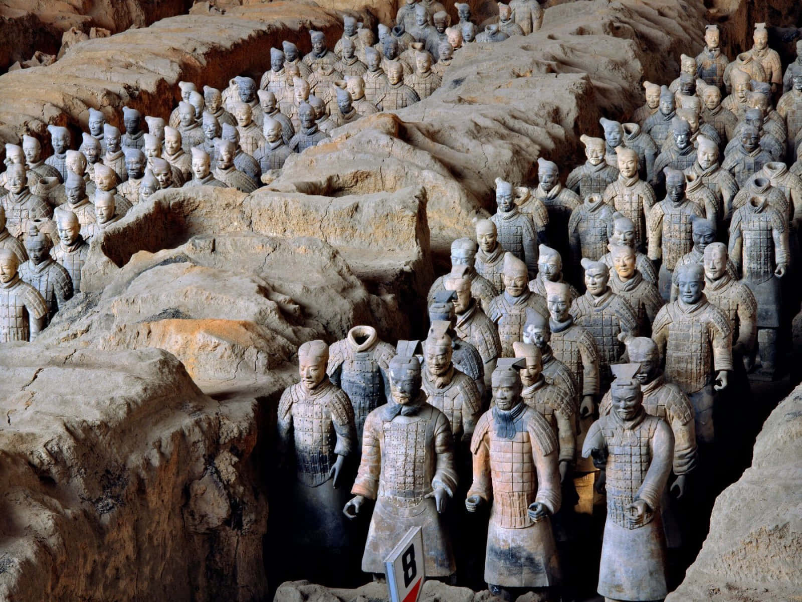 Museum 桌布 壁紙 — 一排排古老的兵馬俑站在泥土的發掘坑中，帶有詳細的盔甲和多樣的表情。