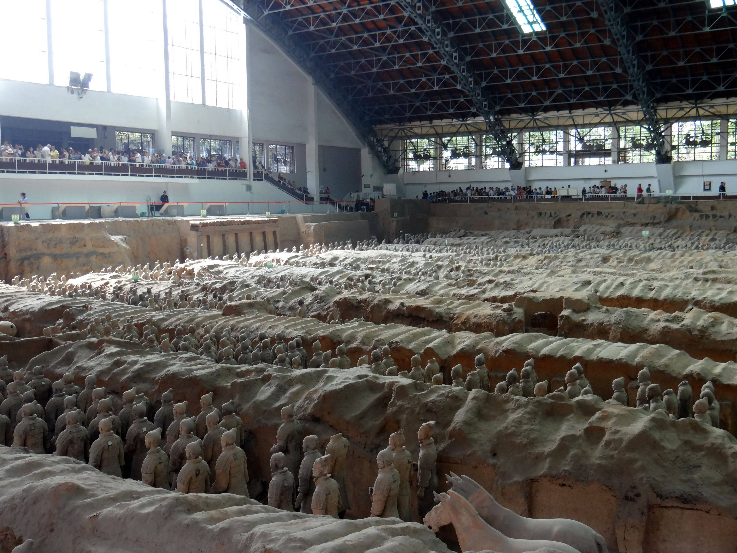 Xian 桌布 壁紙 — 一排排古老的兵馬俑站在現代展覽館下的土坑中，參觀者從陽台上觀看。