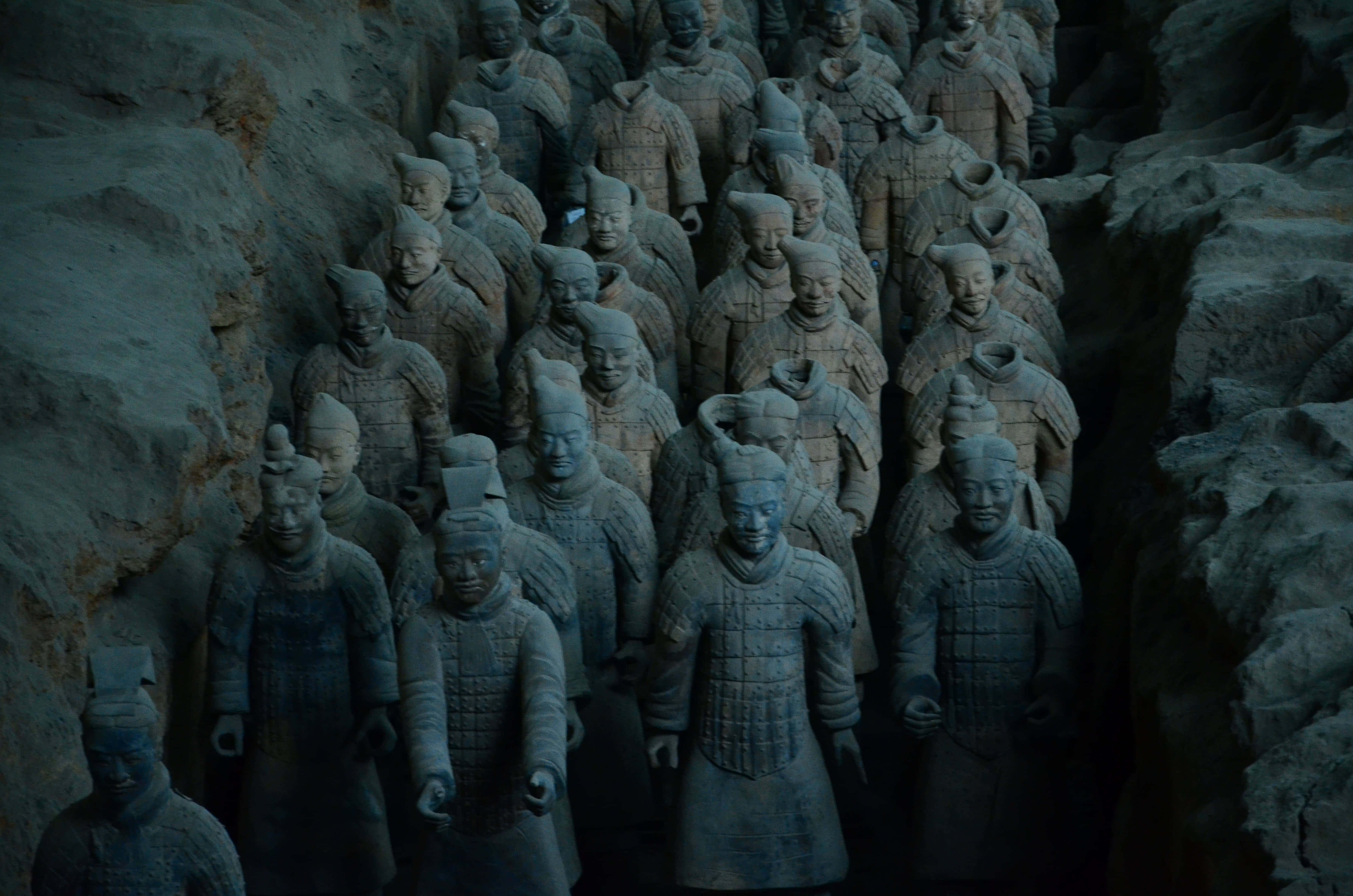 Museum 桌布 壁紙 — 一排排古老的兵馬俑莊嚴地矗立在光線昏暗的地下坑道中，它們的土色盔甲和細緻的臉龐以粗獷的寫實風格呈現。