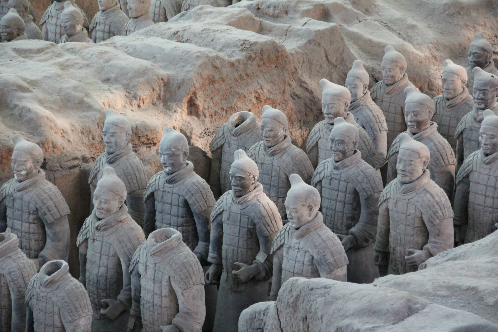 Xian 桌布 壁紙 — 一排排古老的兵馬俑莊嚴地站在他們的發掘坑中，帶有大地色調和詳細的盔甲。