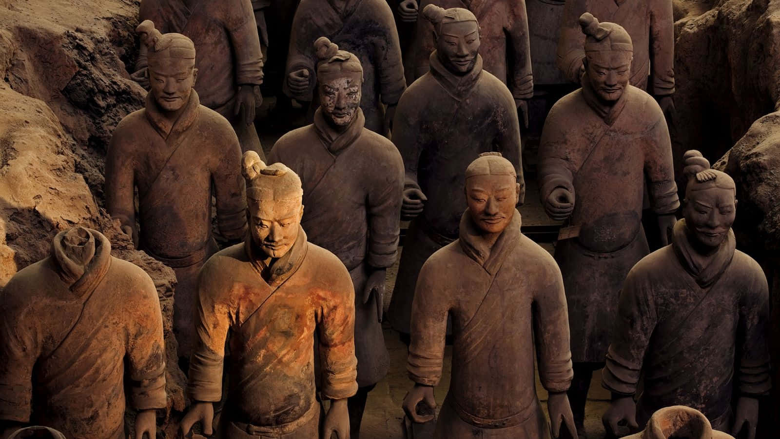 Museum 桌布 壁紙 — 一排排古老的兵馬俑莊嚴地站立在泥土的墓坑中，帶有細緻的面部表情和風化的陶土紋理。