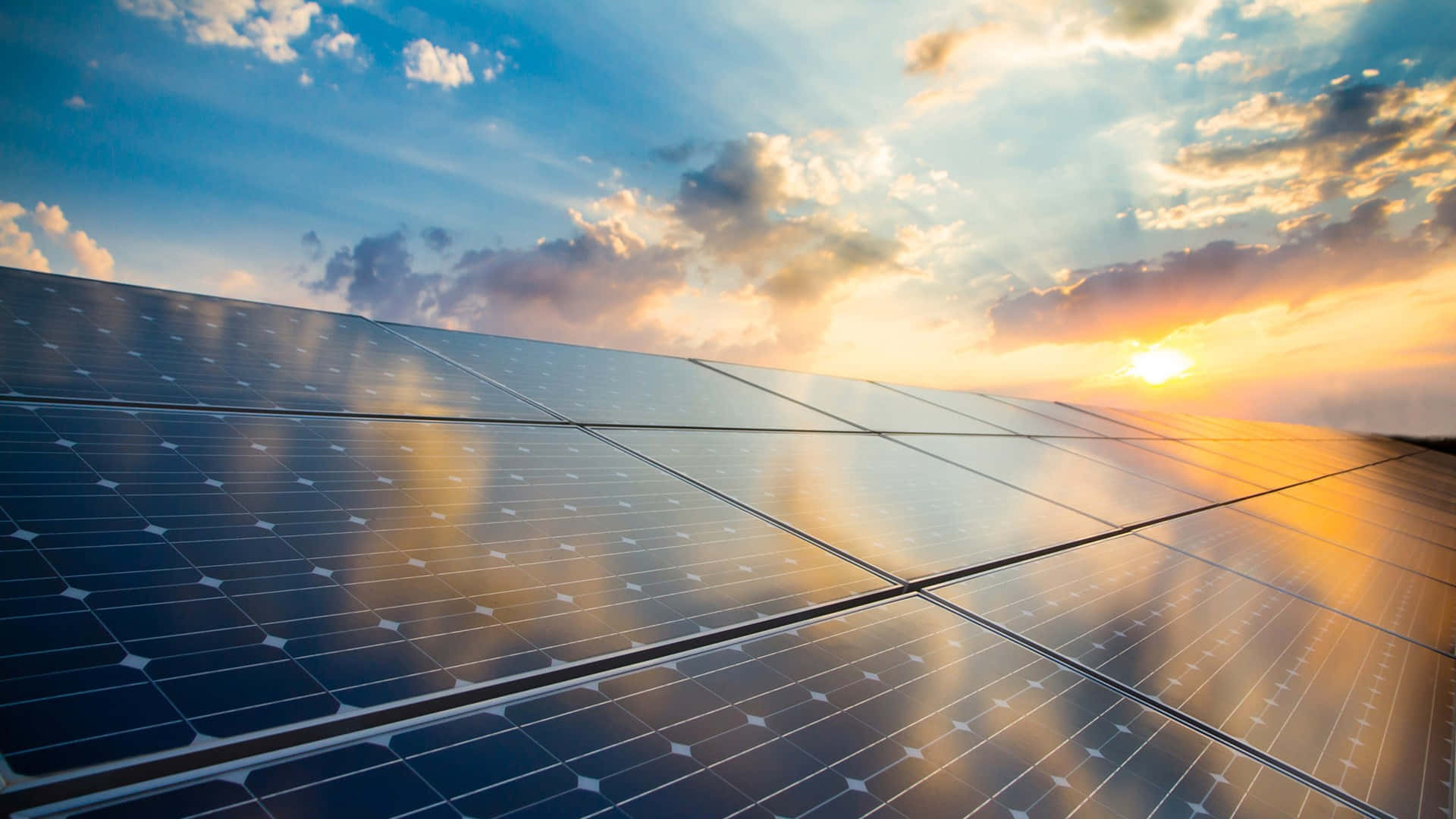 Solar Panel 桌布 壁紙 — 一排排太陽能板反射出充滿活力的日落天空，帶有金色雲彩和藍色漸變。