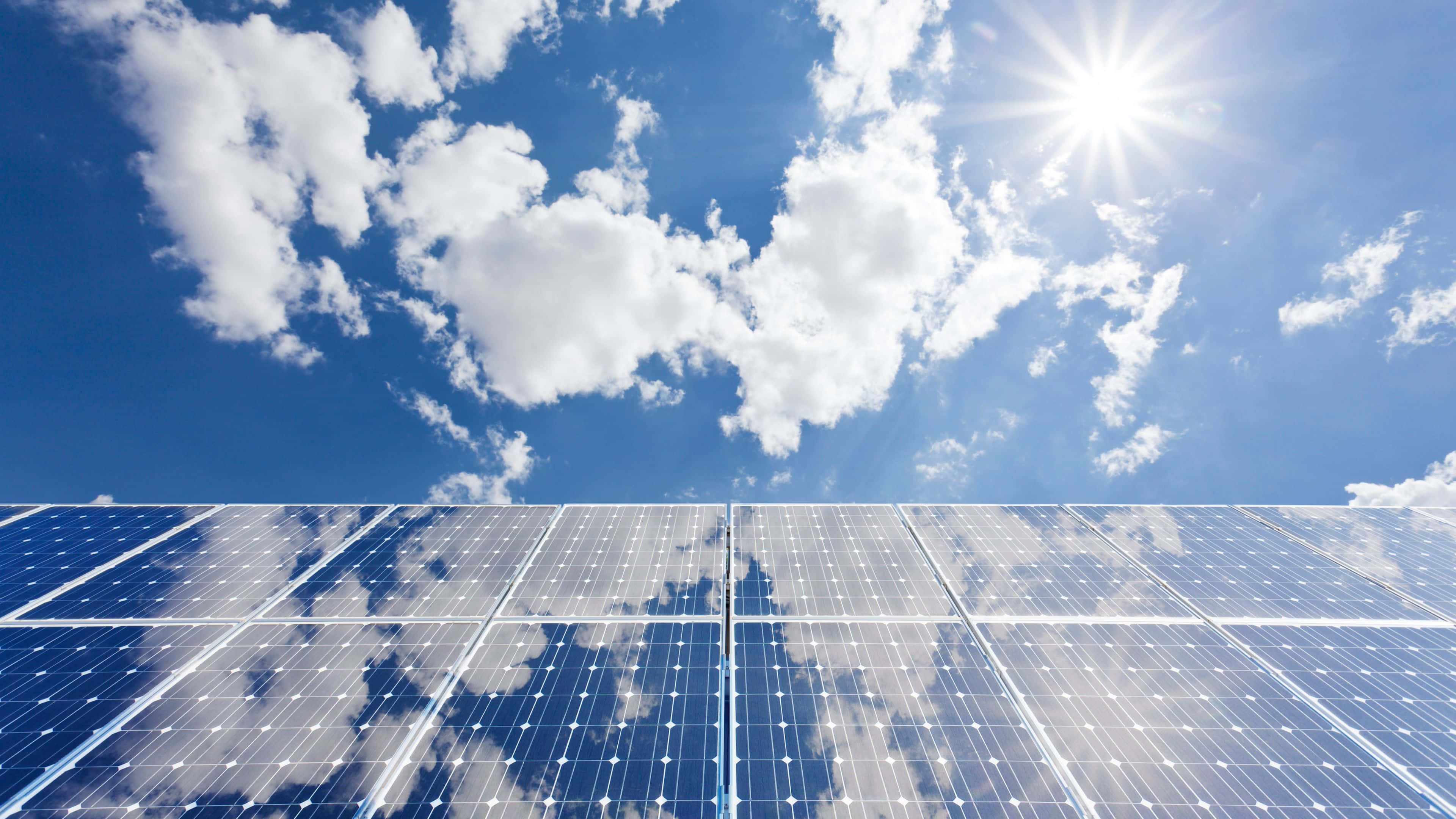 Solar Panel 桌布 壁紙 — 一排排太陽能板反射出明亮的藍天，點綴著蓬鬆的白雲和燦爛的太陽。