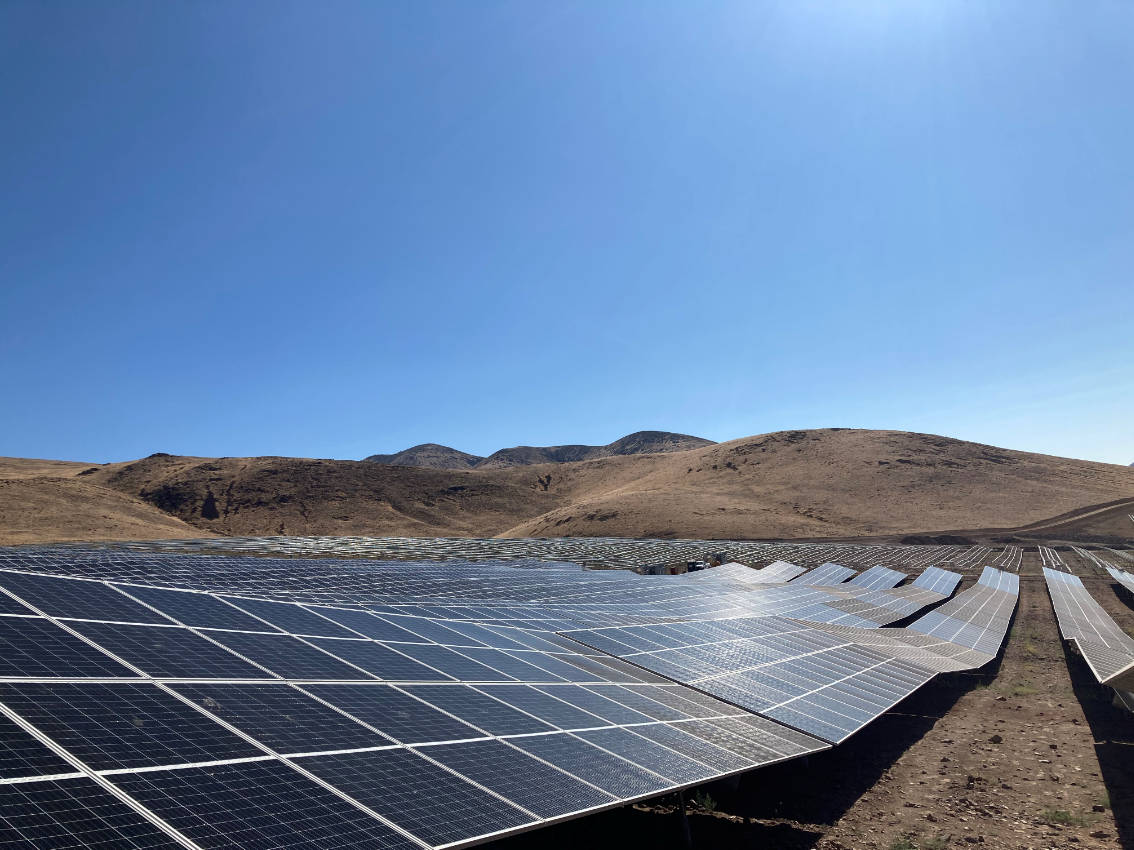 Electricity 桌布 壁紙 — 一排排太陽能板在乾燥的景觀中延伸，背景是晴朗的藍天和遠山。