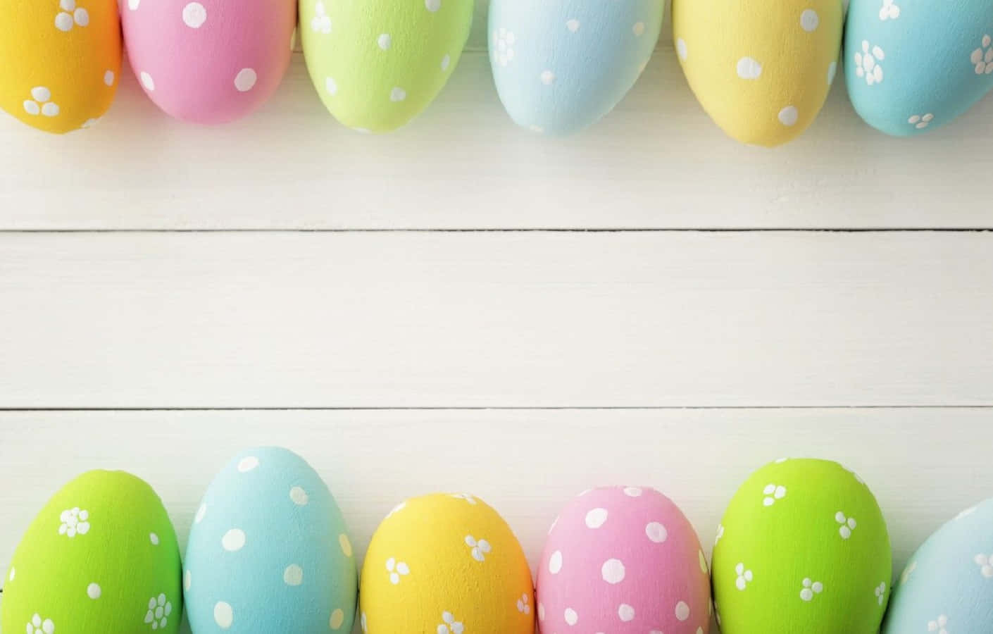 Pastel Easter 桌布 壁紙 — 一排排帶有白色圓點和花卉圖案的柔和色調復活節彩蛋，放置在白色木質表面上。