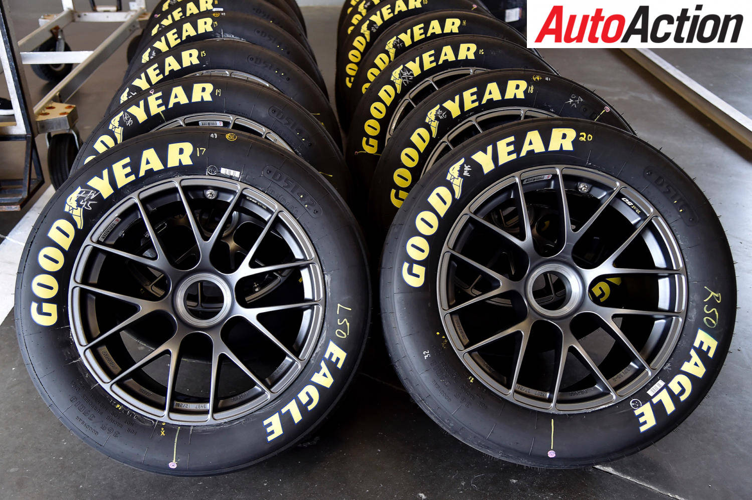 Racing 桌布 壁紙 — 一排排帶有黑色輪圈和粗體黃色字樣的Goodyear Eagle賽車輪胎整齊地放在車庫中。