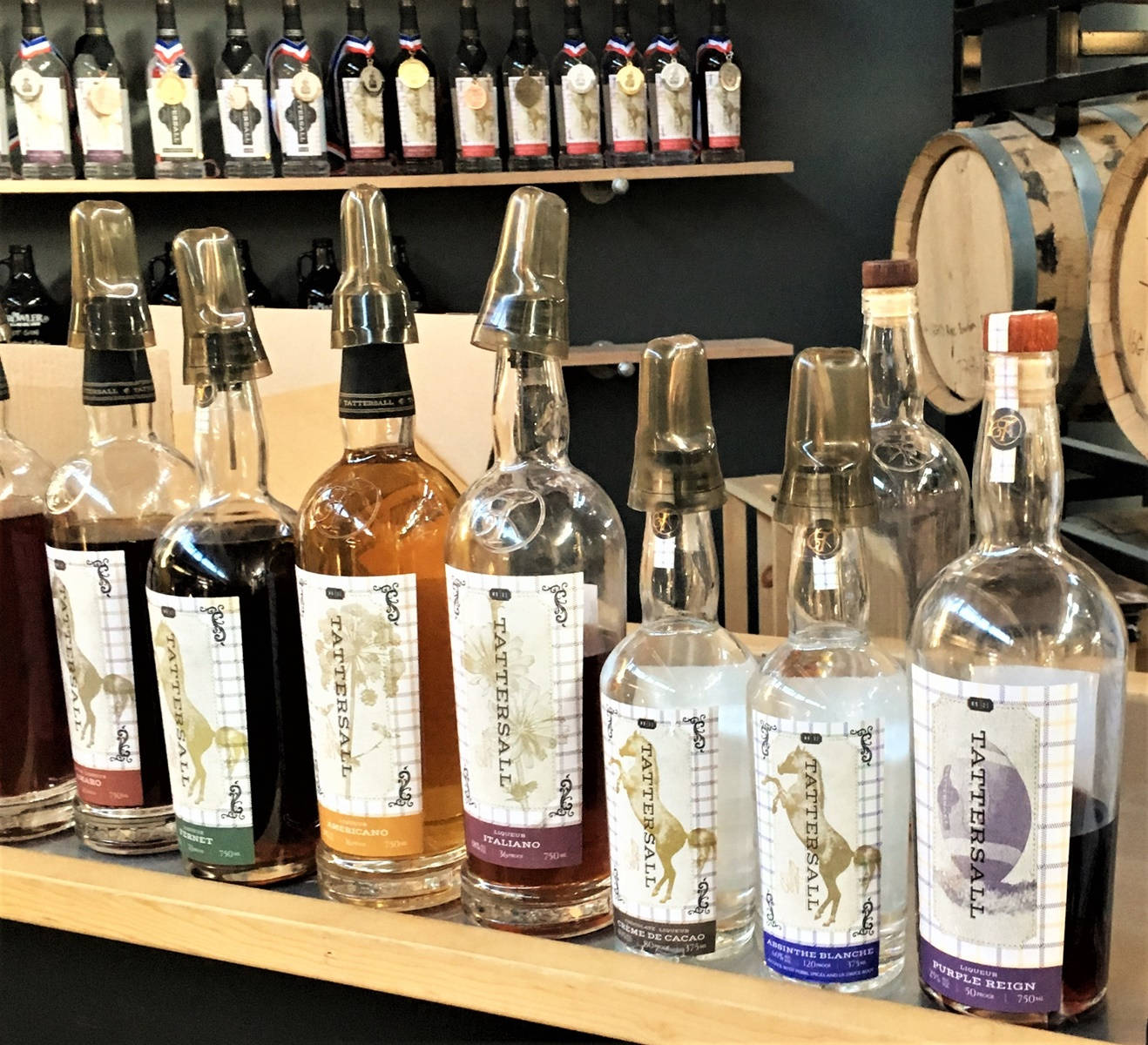 Drink 桌布 壁紙 — 一排排帶金屬蓋的Tattersall酒瓶放在木架上，旁邊是酒桶，位於鄉村風格的釀酒廠。