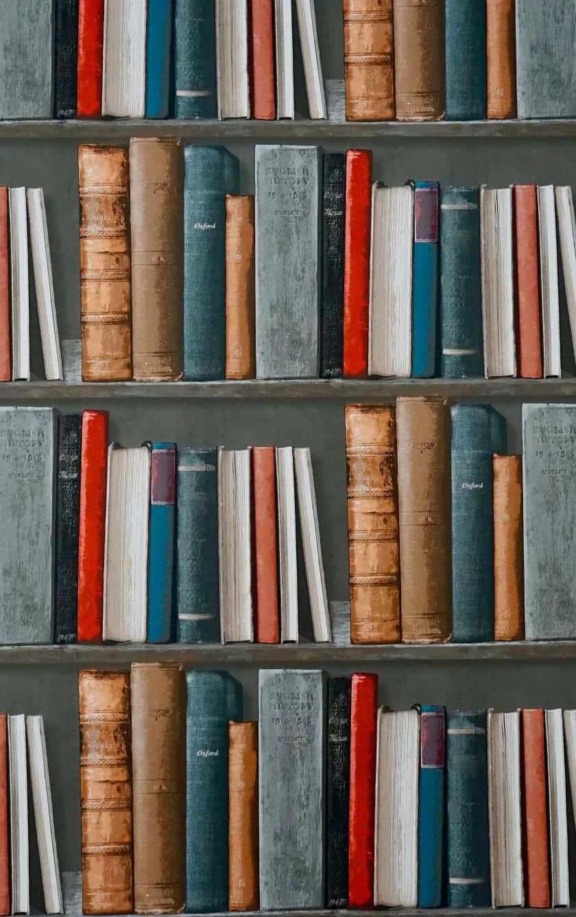Library 桌布 壁紙 — 一排排復古書籍，帶有磨損的皮革和布質書脊，以大地色調排列在深色木架上。