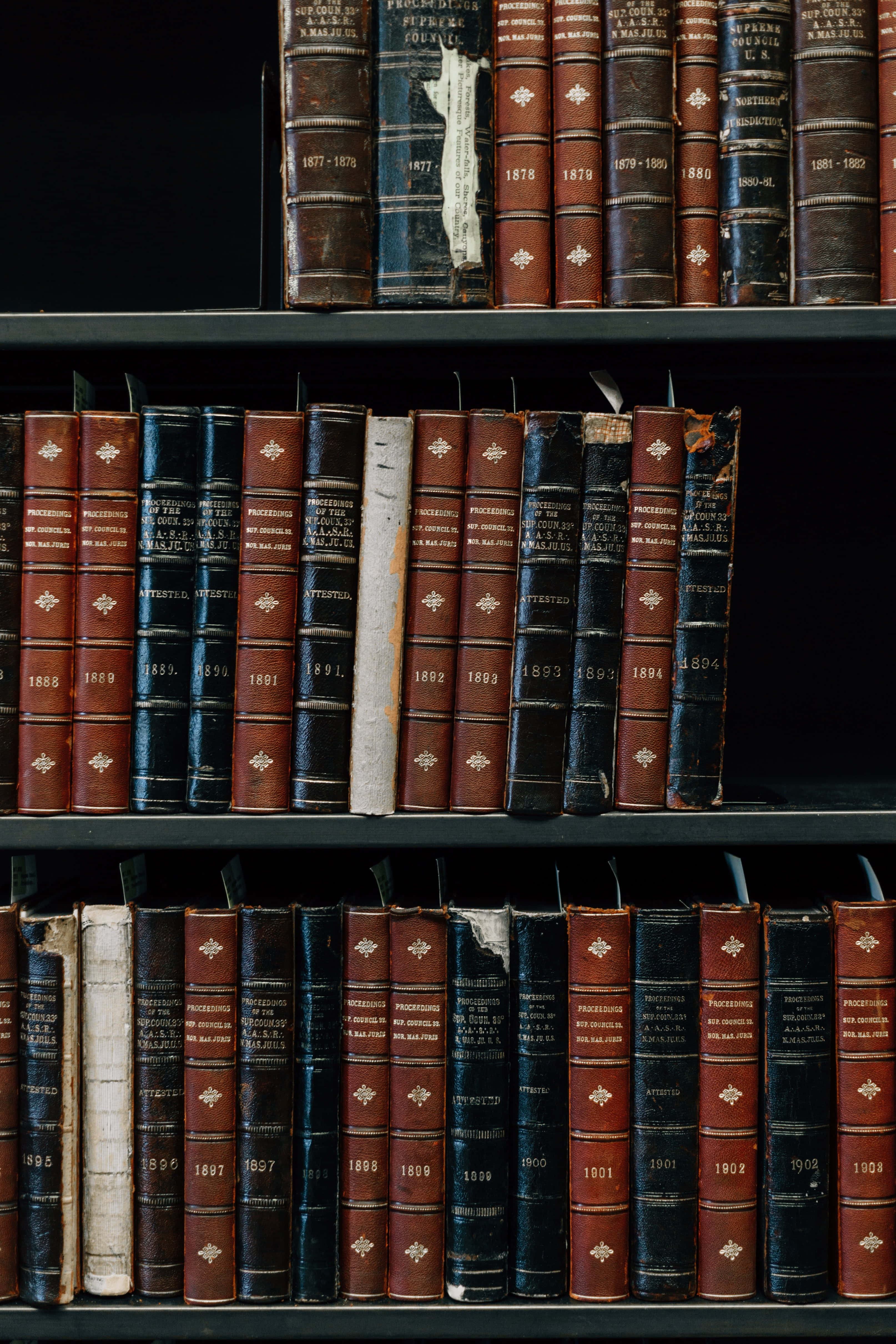 Library 桌布 壁紙 — 一排排復古皮革裝訂書籍，帶有金色壓印標題和日期，排列在安靜圖書館的深色木書架上。