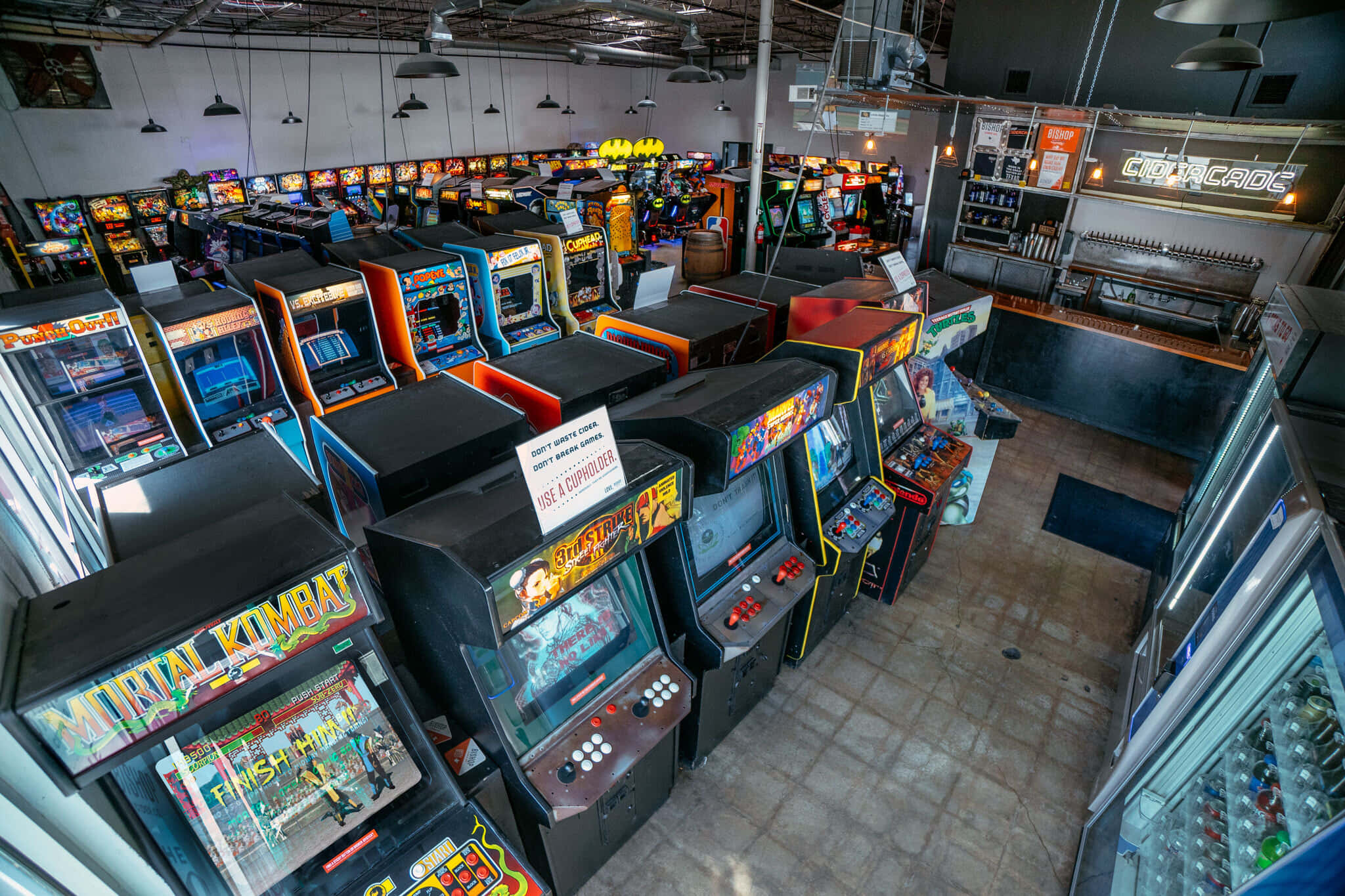 Arcade Games 桌布 壁紙 — 一排排復古街機，帶有發光螢幕和色彩繽紛的機櫃，在裸露的天花燈光下充滿了復古遊戲廳。