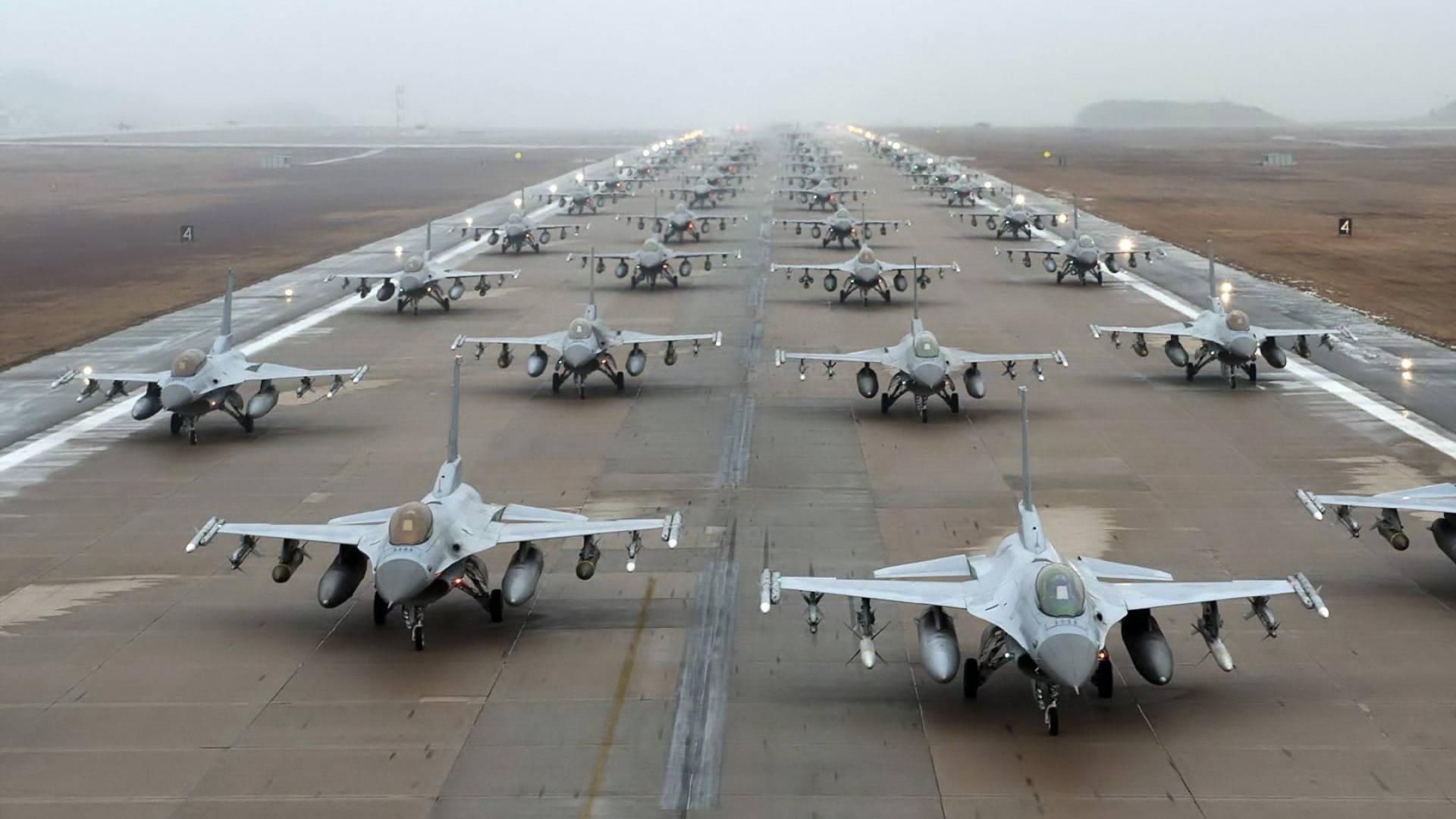 Runway 桌布 壁紙 — 一排排戰鬥機排列在潮濕的停機坪上，天空灰濛濛，遠方有山丘。