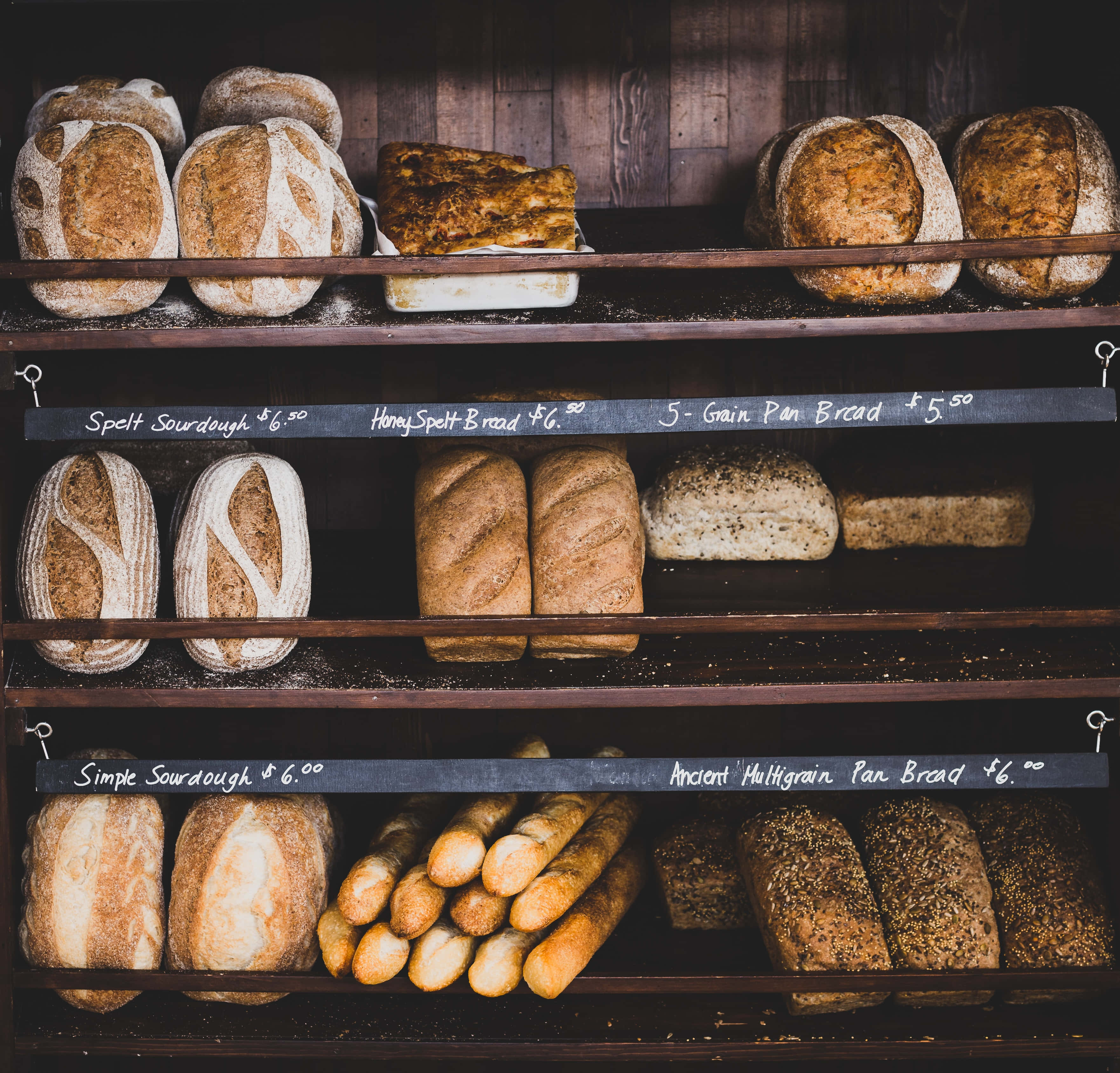 Bakery 桌布 壁紙 — 一排排手工麵包，帶有鄉村風格外皮，陳列在麵包店的深色木架上。