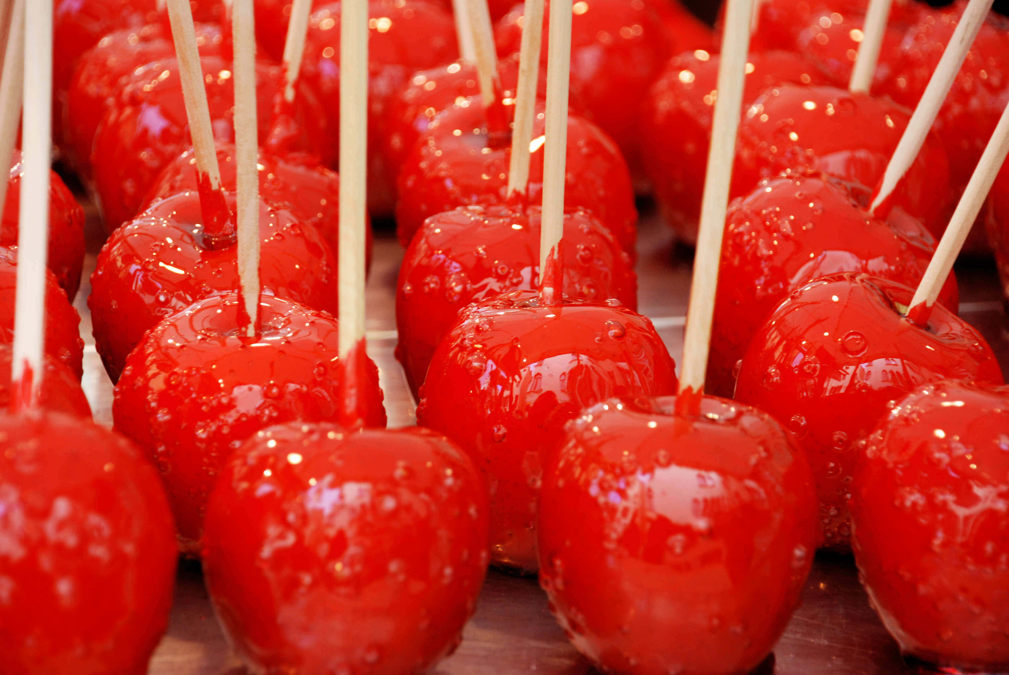 Candy Apples 桌布 壁紙 — 一排排插在木棒上的亮紅色糖蘋果，在特寫鏡頭中閃爍著糖滴的光澤。
