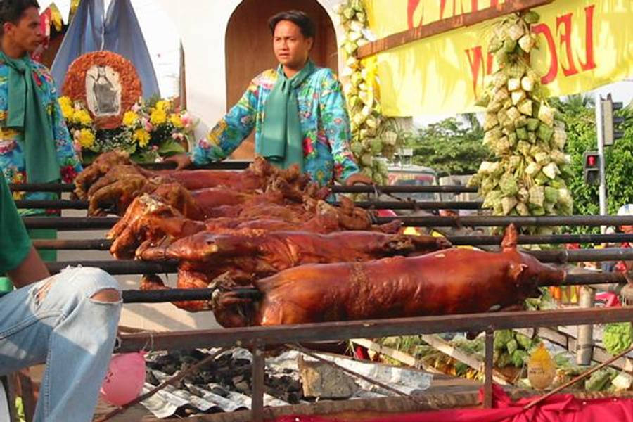 Pig 桌布 壁紙 — 一排排整隻烤豬在金屬烤叉上閃閃發光，位於一個裝飾著鮮花和橫幅的充滿活力的戶外美食攤位。