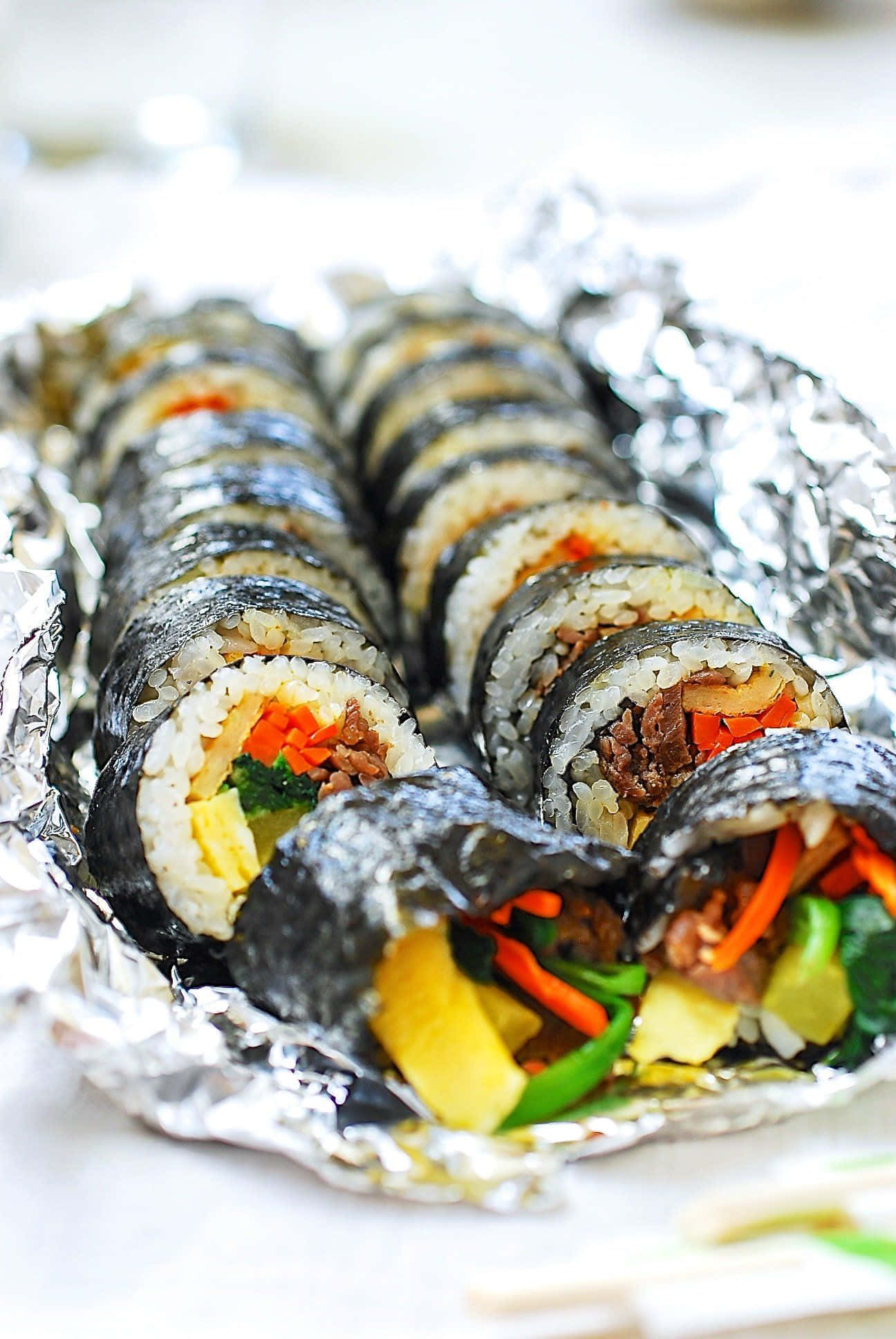 Seaweed 桌布 壁紙 — 一排排新鮮製作的韓國紫菜飯捲，裡面有色彩繽紛的蔬菜和肉，放在皺巴巴的鋁箔紙上。