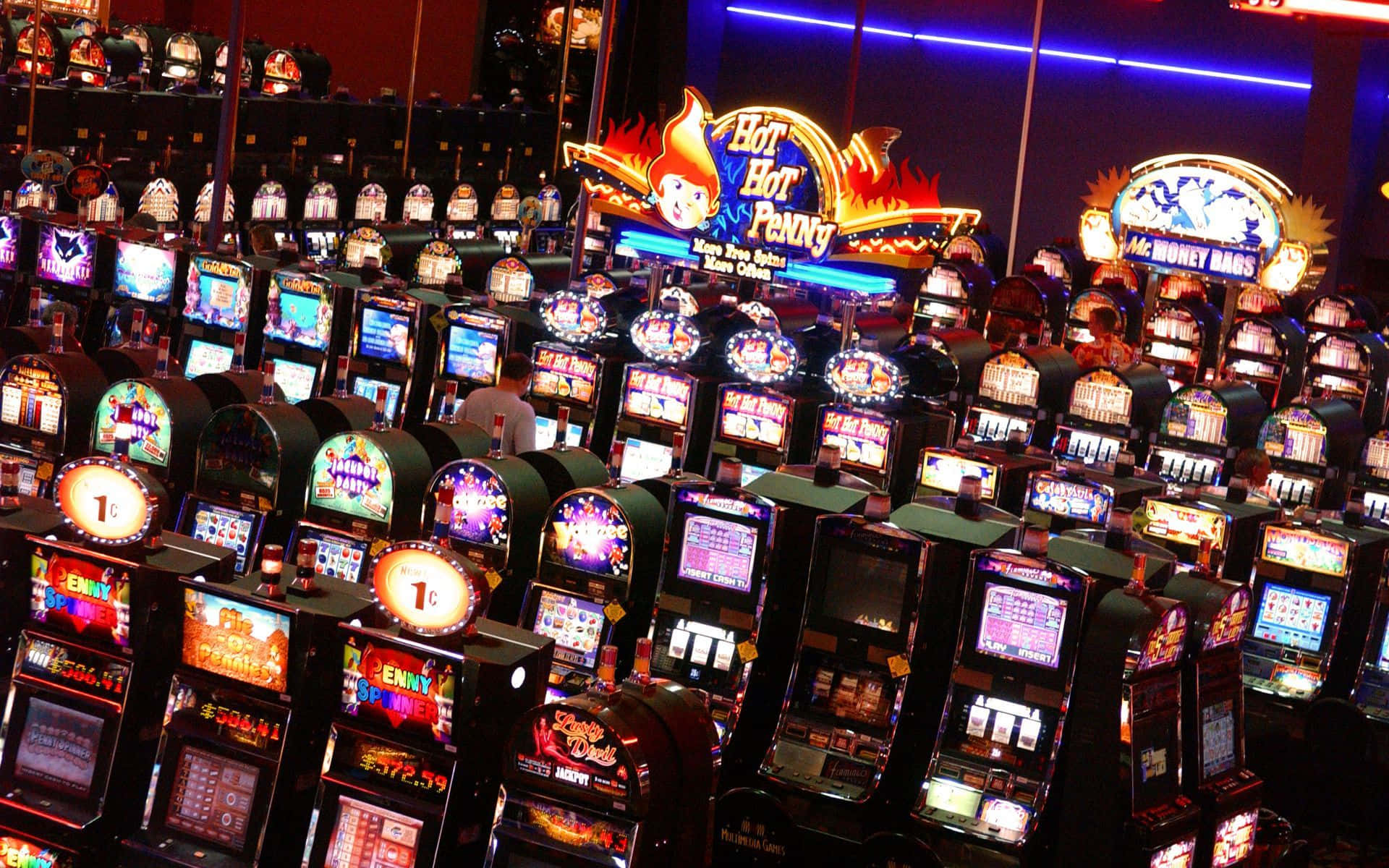 Slot Machine 桌布 壁紙 — 一排排明亮照明的老虎機在擁擠的賭場地板上，在霓虹燈招牌下閃耀。