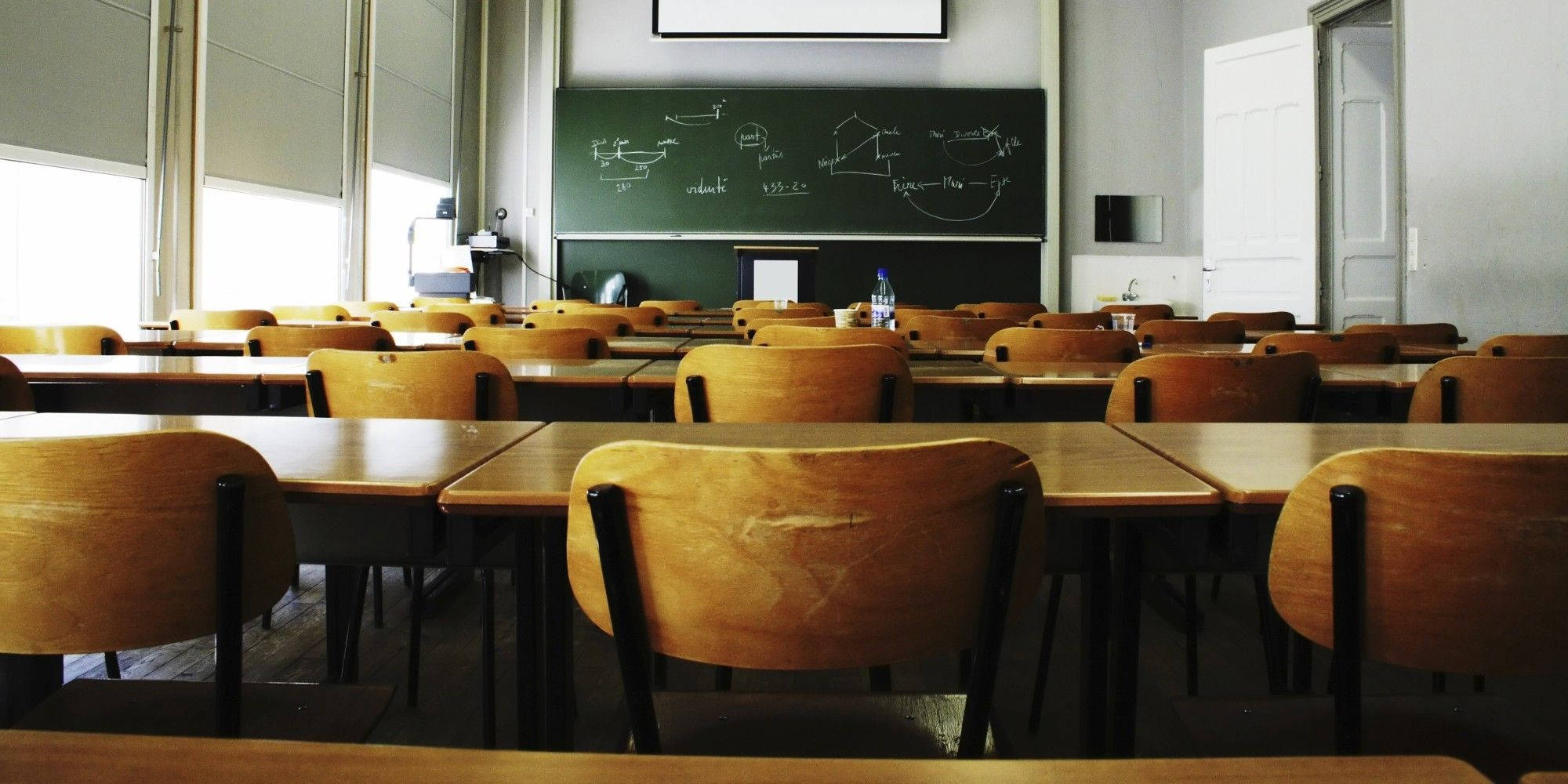 Chalkboard 桌布 壁紙 — 一排排木製書桌和椅子面向一塊充滿物理方程式的黑板，空無一人的教室沐浴在自然光中。