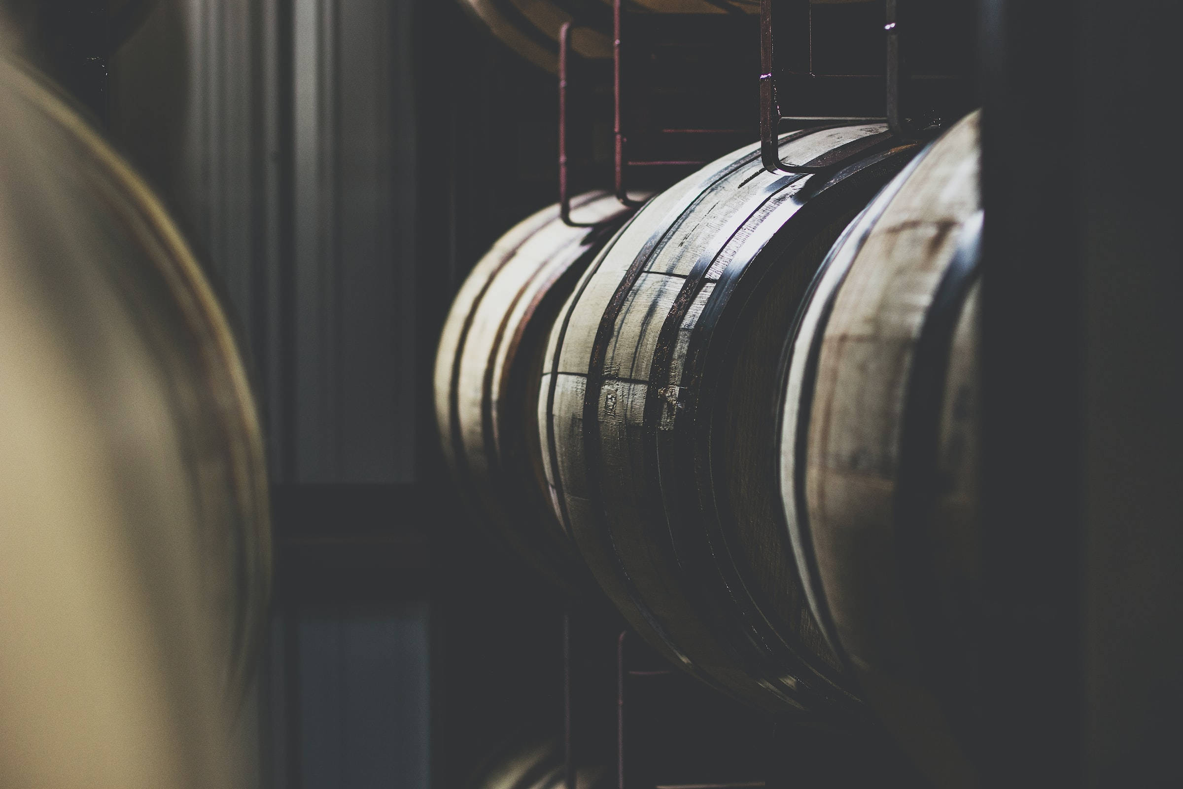 Beer 桌布 壁紙 — 一排排木製葡萄酒桶在昏暗光線中矗立於質樸的酒窖內，其彎曲表面捕捉柔和陰影。