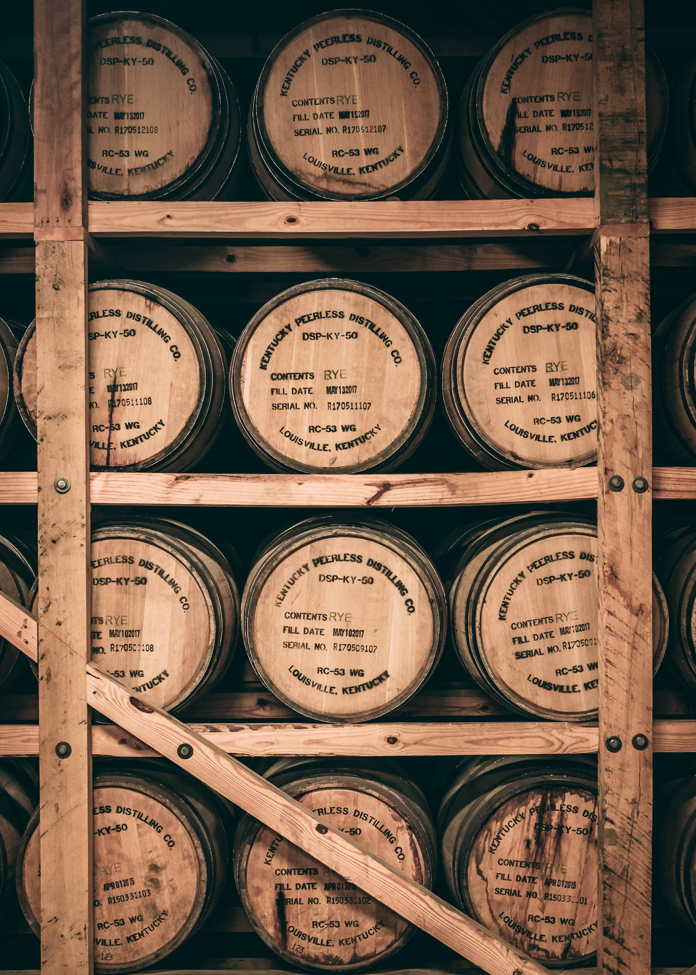 Beer 桌布 壁紙 — 一排排標有 'Kentucky Peerless Distilling Co' 的木製波本桶堆疊在一個帶有溫暖琥珀色照明的質樸倉庫中。