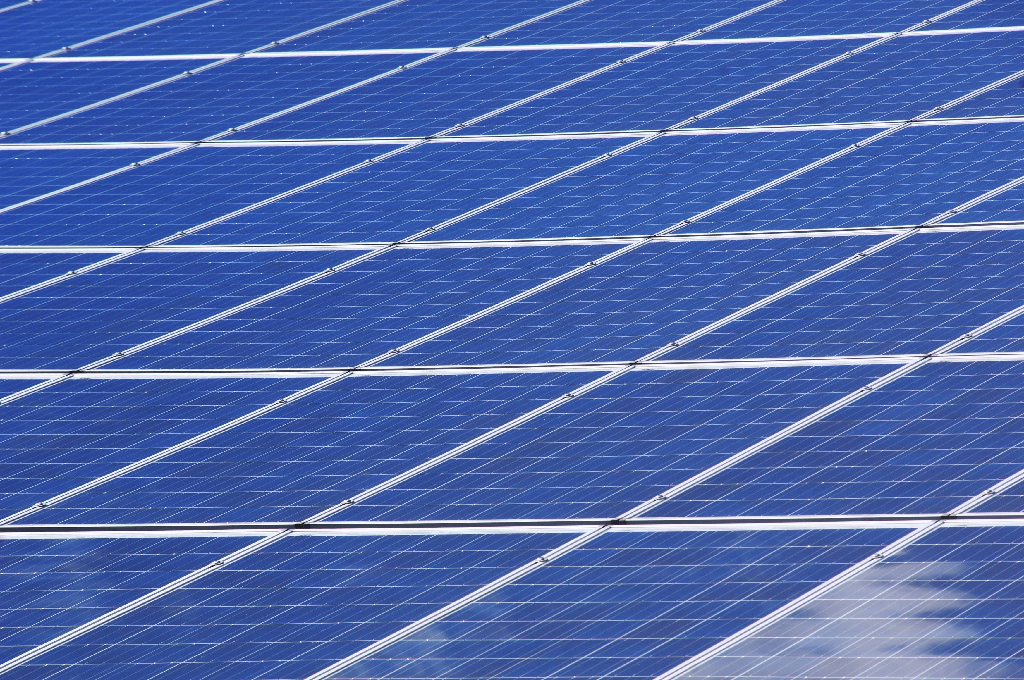 Solar Panel 桌布 壁紙 — 一排排深藍色太陽能板帶有白色網格線，反射出明亮的天空。