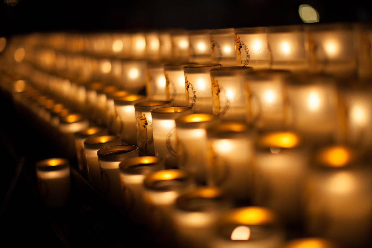 Condolence 桌布 壁紙 — 一排排發光的蠟燭在玻璃燭台中，在昏暗的空間中營造出溫暖寧靜的氛圍。