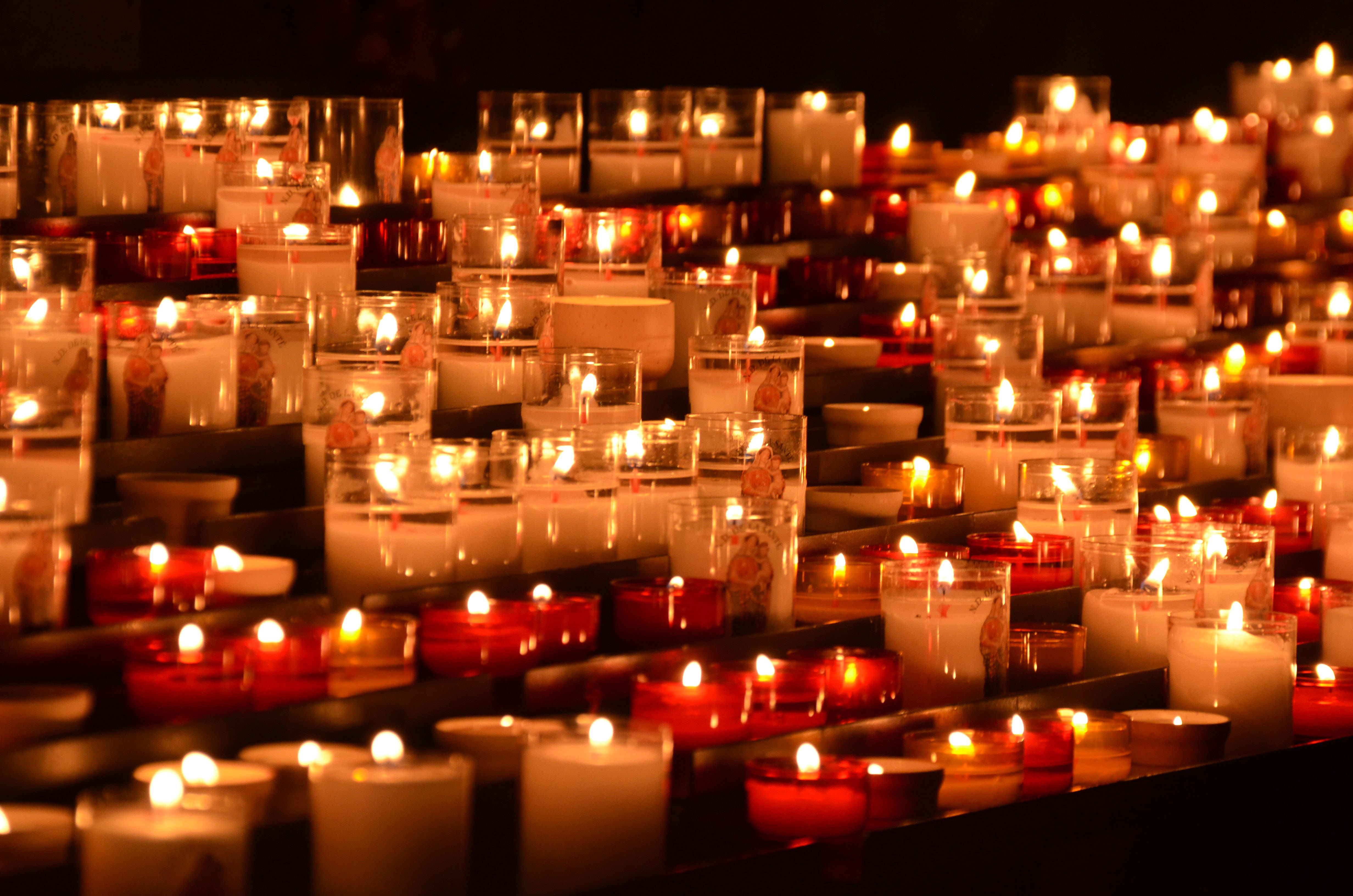 All Saints Day 桌布 壁紙 — 一排排發光的蠟燭在玻璃燭台中，在黑暗背景下投射出溫暖的琥珀色光芒。