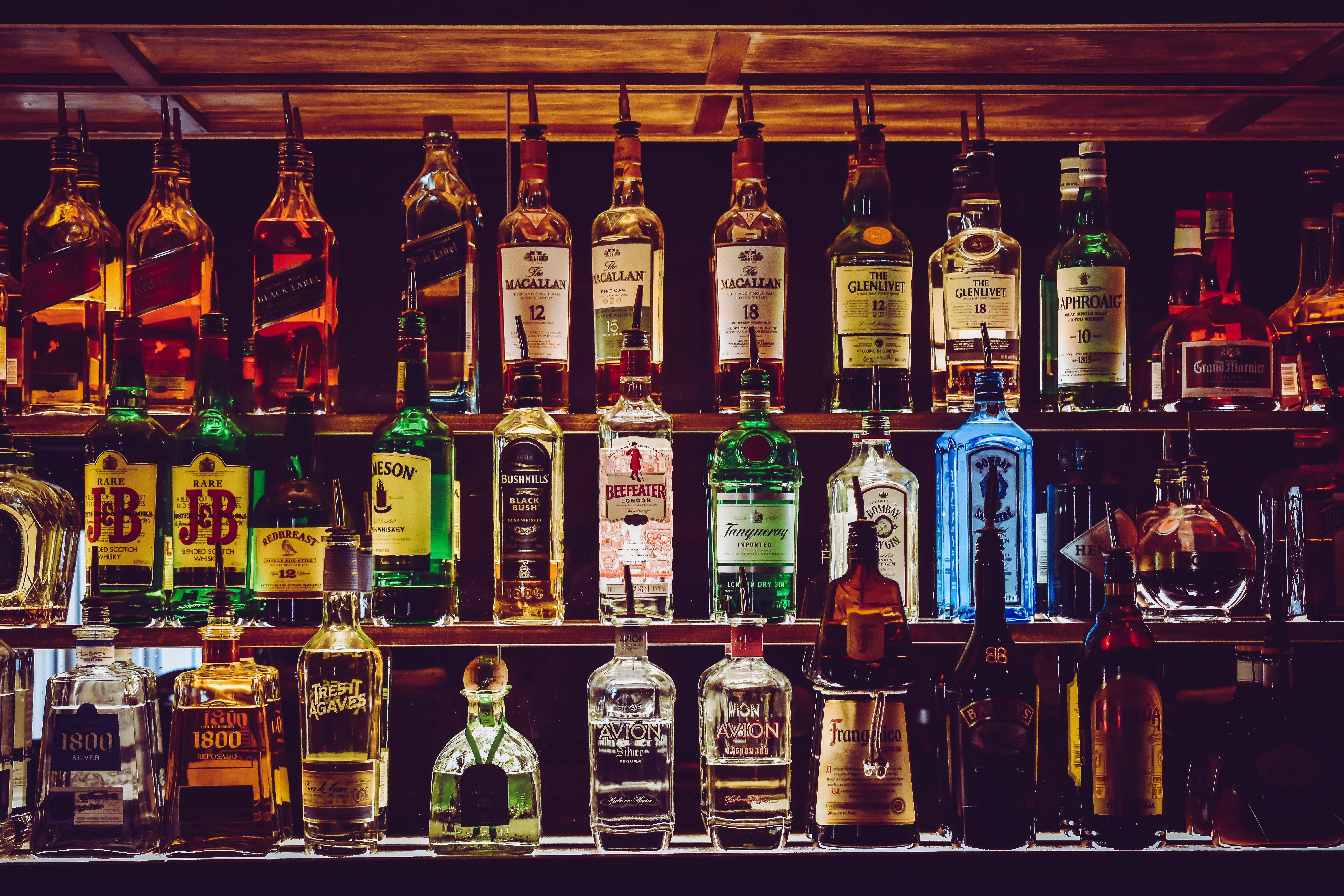 alcohol 桌布 壁紙 — 一排排發光的酒瓶排列在昏暗的酒吧架子上，上方是溫暖的木樑。