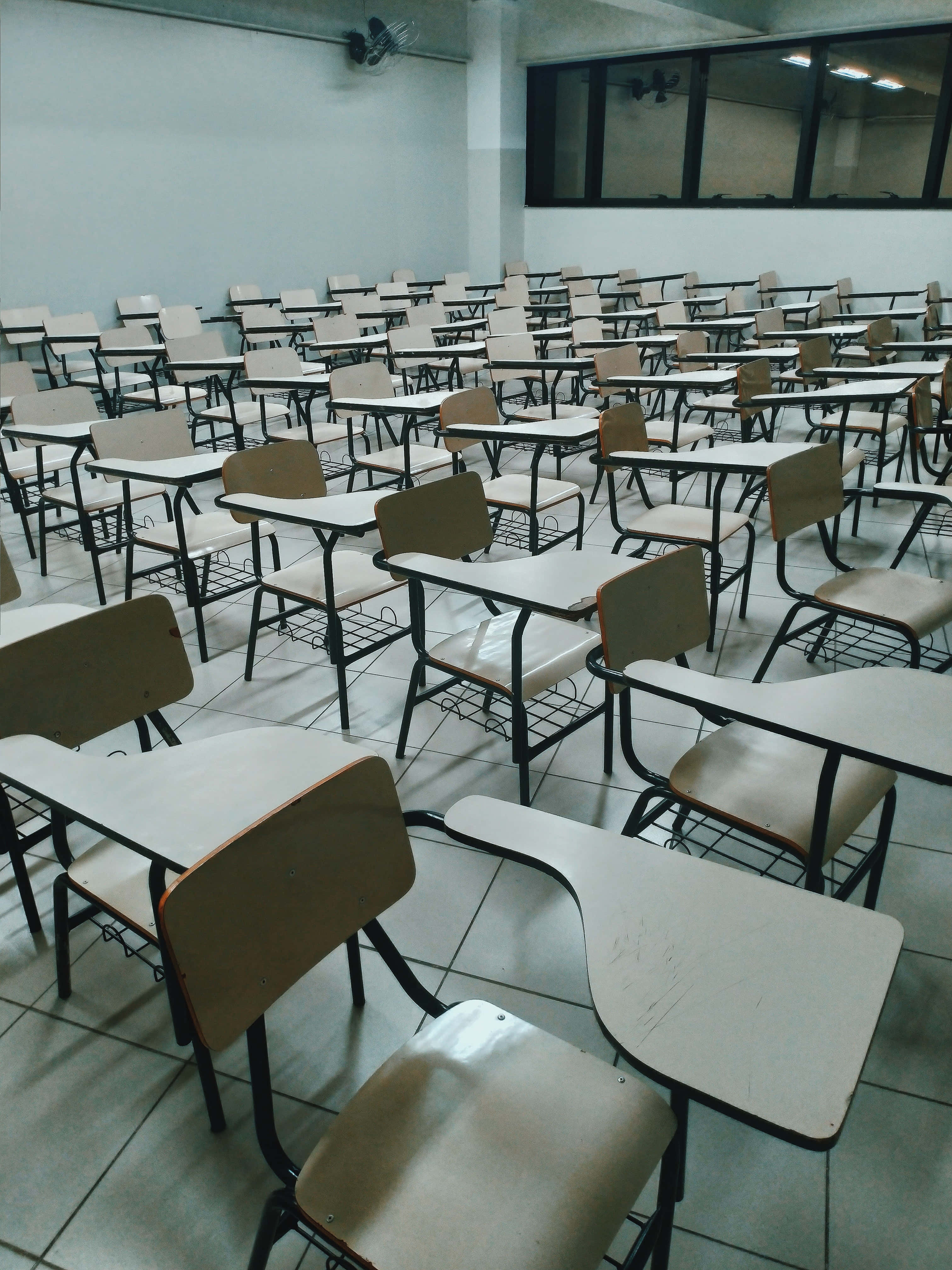 Classroom 桌布 壁紙 — 一排排空的木製書桌和椅子填滿了一個安靜、螢光燈照明的教室，地板鋪有瓷磚，窗戶寬大。