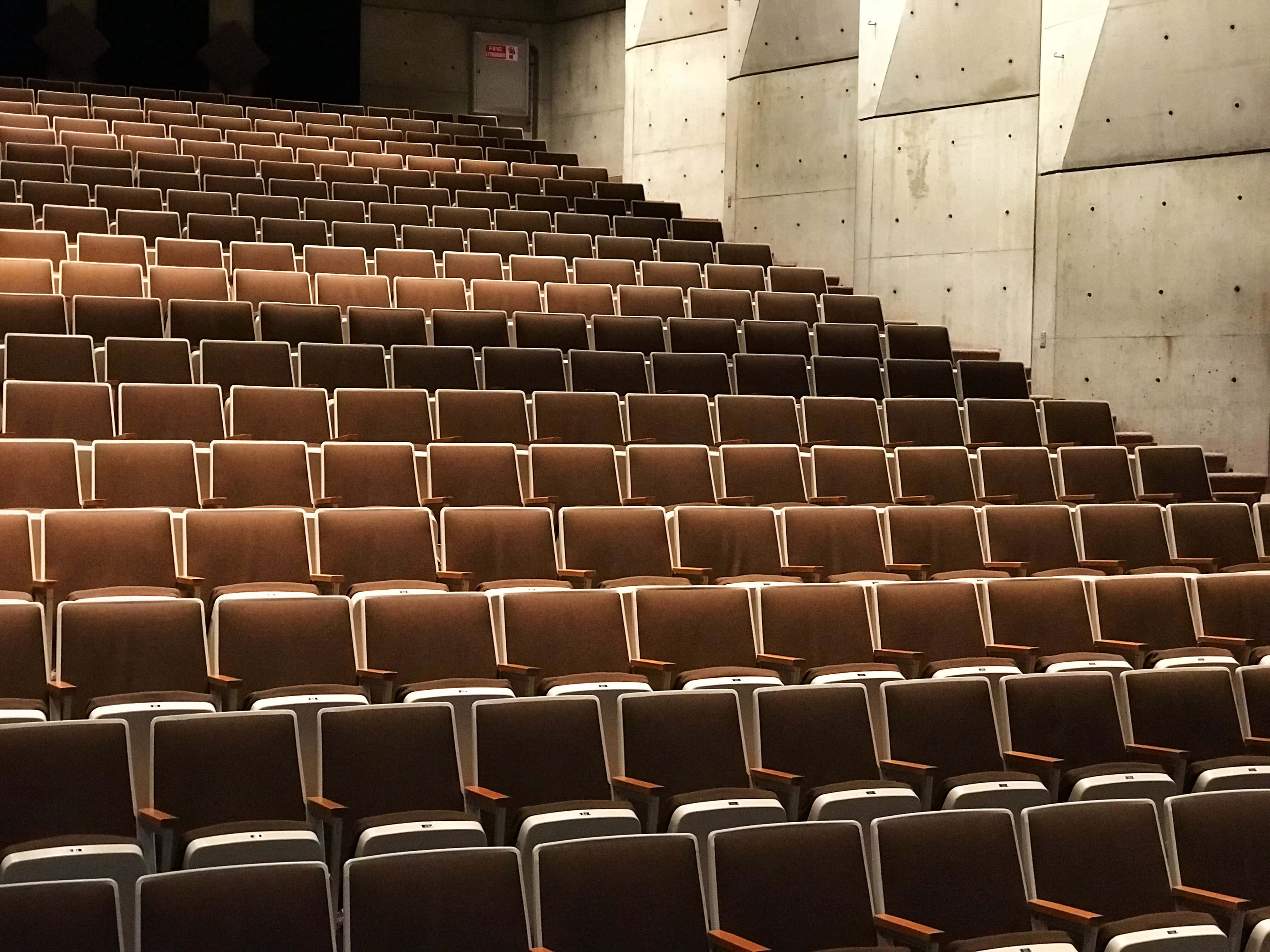 seat 桌布 壁紙 — 一排排空的棕色劇院座位在溫暖的環境光線下向混凝土牆上升。