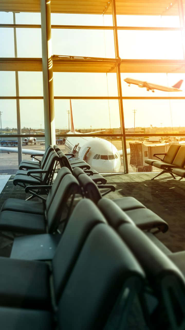 Airport 桌布 壁紙 — 一排排空置的機場座位面向大窗，一架飛機在金色日落時分降落。