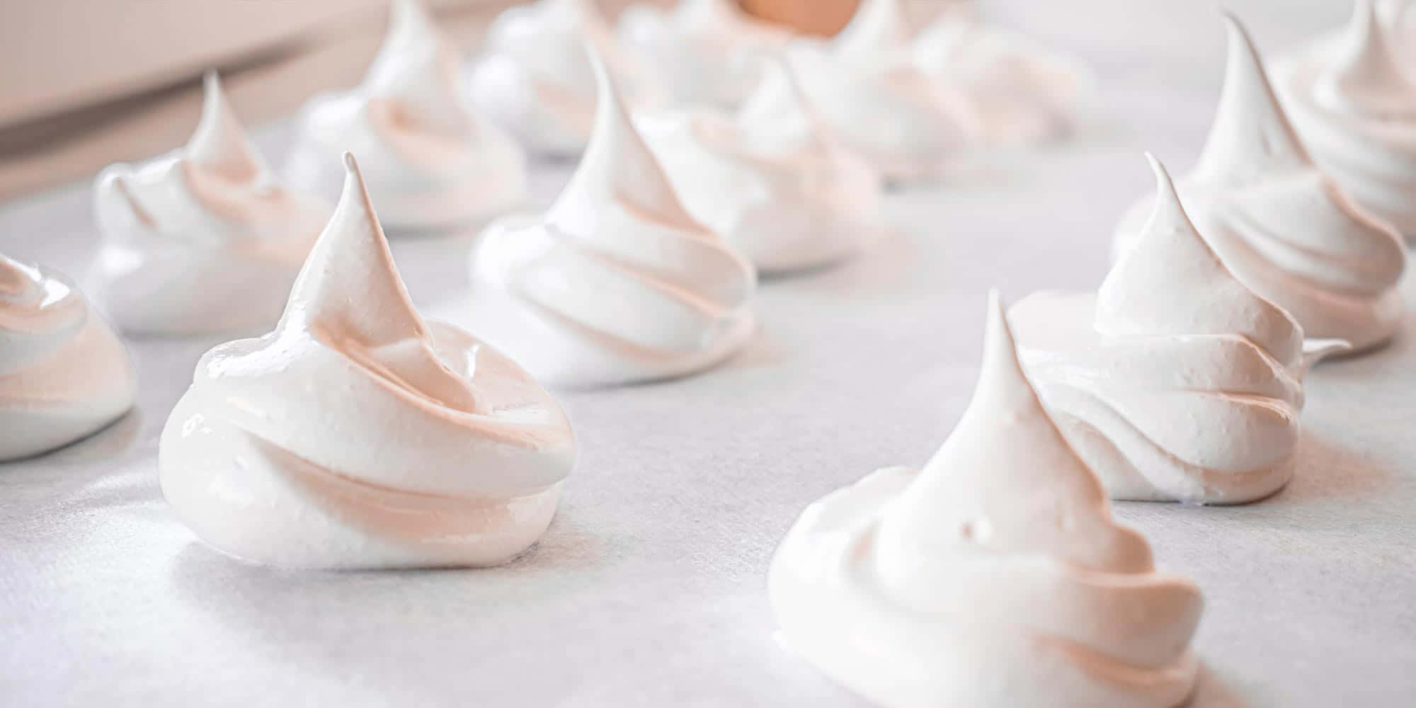 Meringue 桌布 壁紙 — 一排排精緻的白色蛋白霜餅乾，帶有柔和粉紅色，整齊地放在烘焙紙上。
