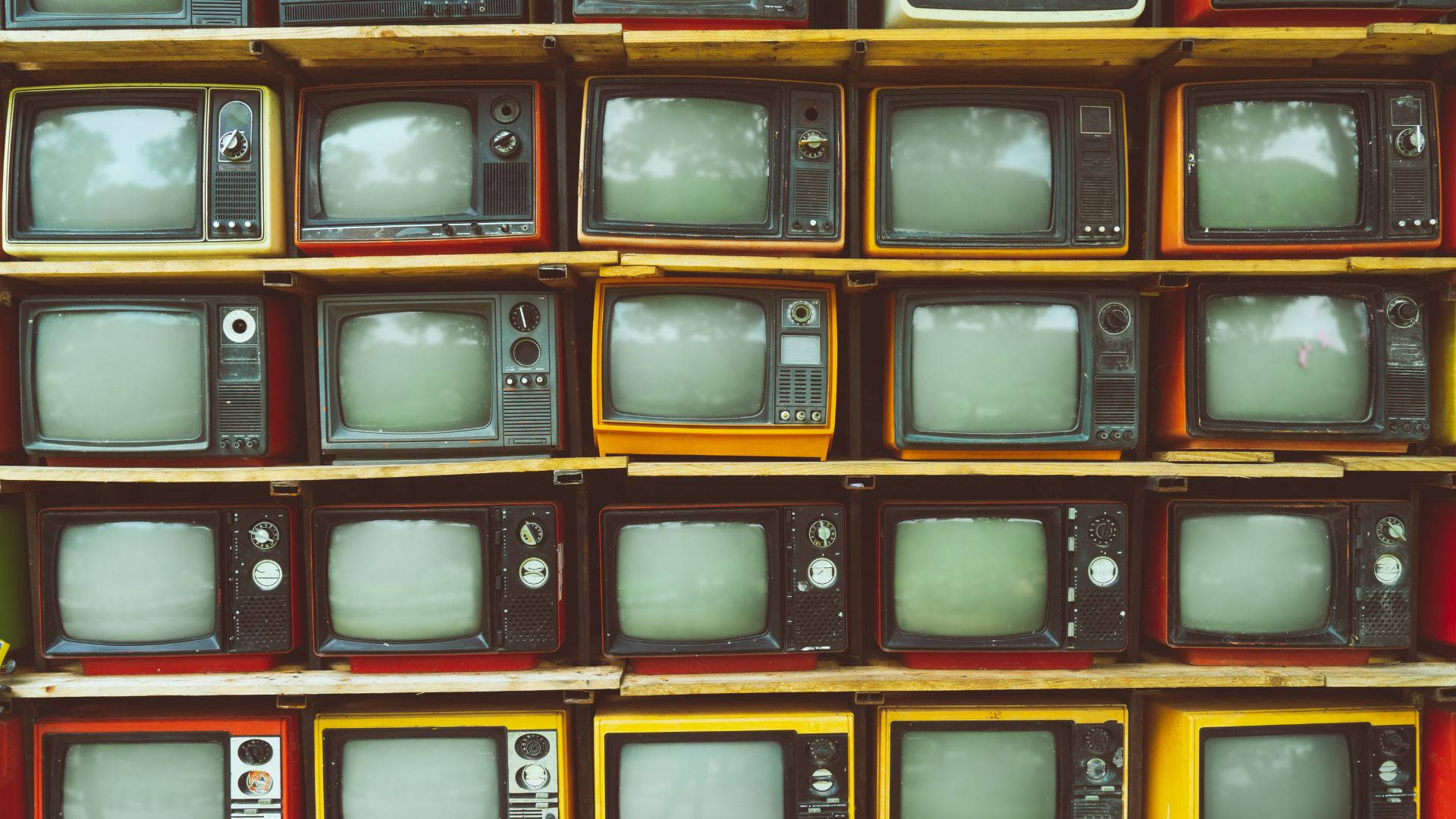 tv 桌布 壁紙 — 一排排紅色、黃色和黑色的復古電視整齊地放在木架上，顯示出柔和的綠色螢幕。
