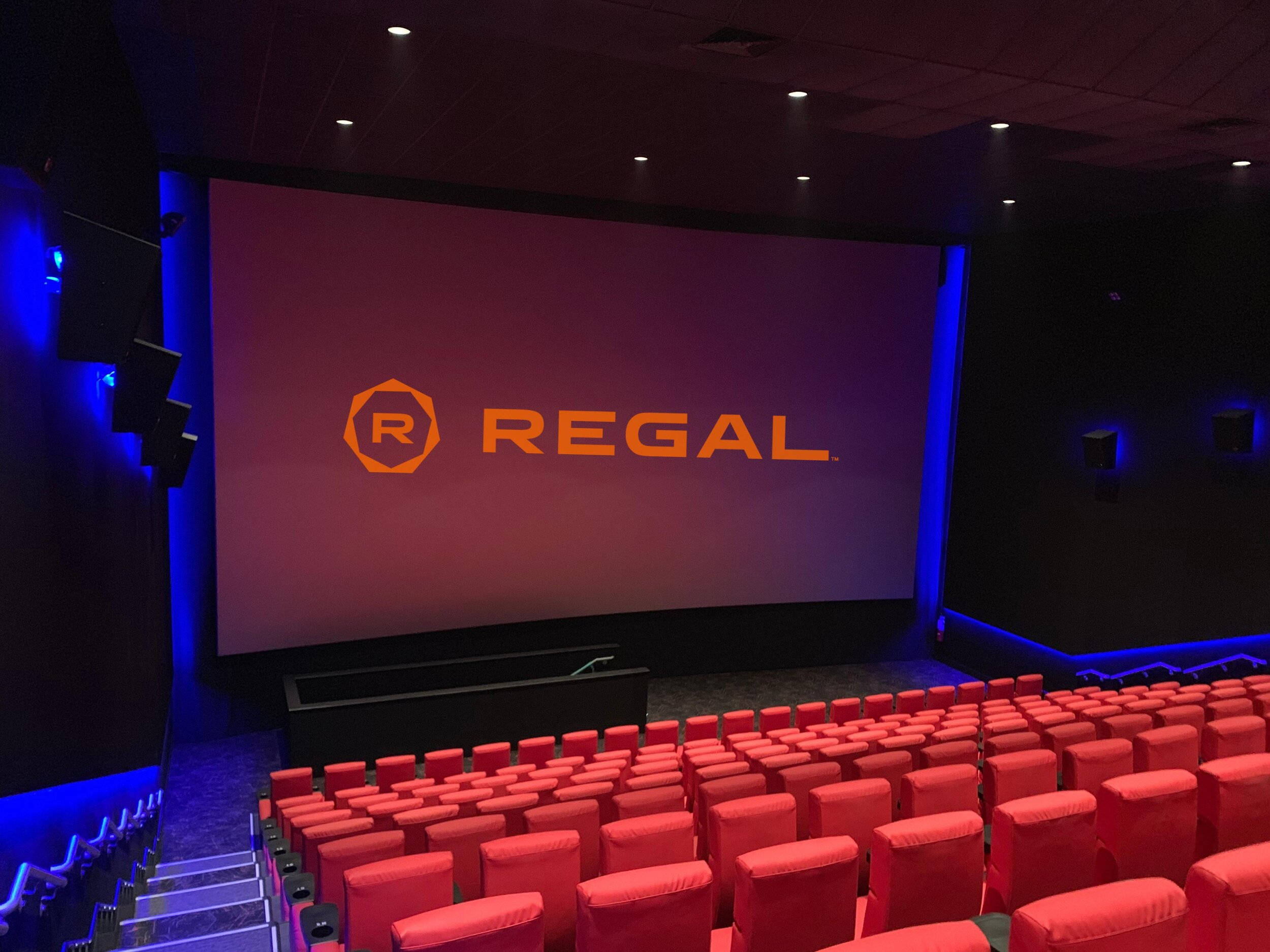 Regal 桌布 壁紙 — 一排排紅色劇院座位面向一個大螢幕，螢幕在藍色環境燈光下顯示Regal標誌。